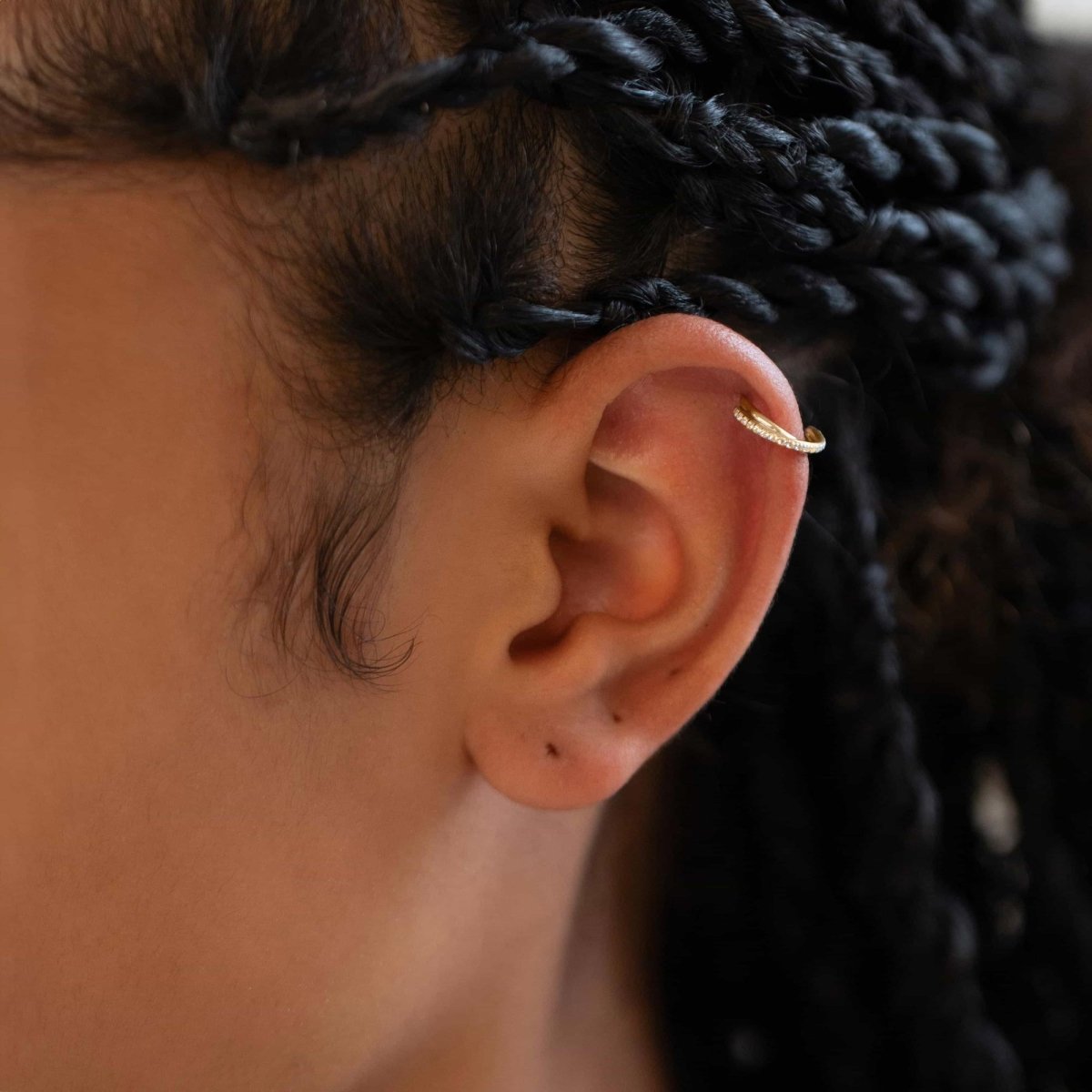 Gold titanium criss cross pavé cartilage hoop with clear stones, shown on a model's helix