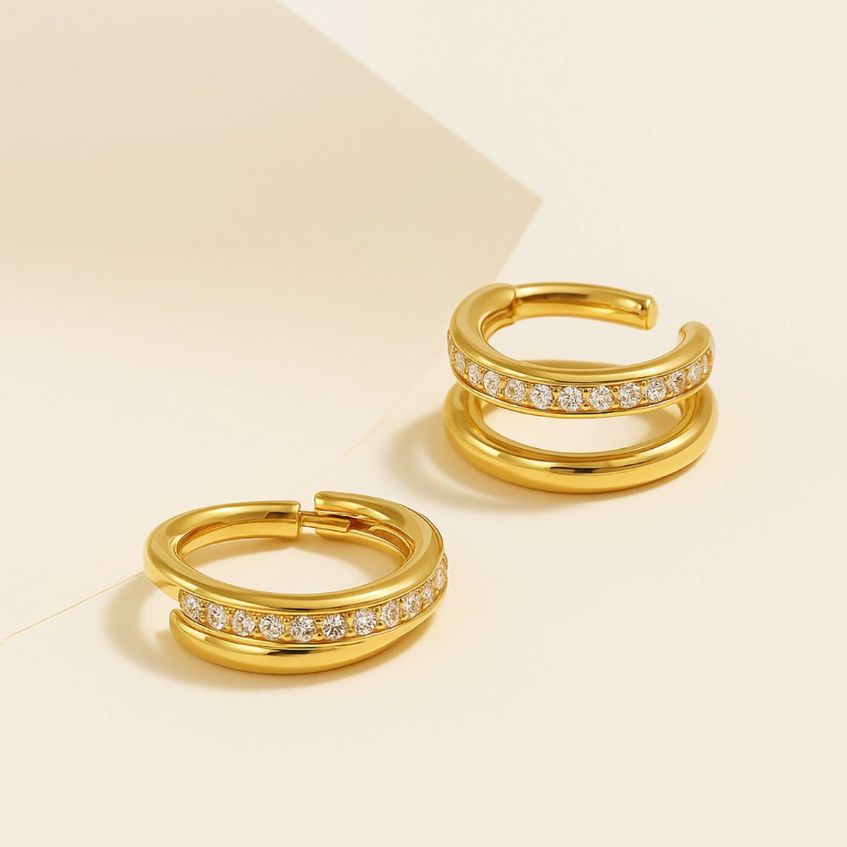 Pair of gold double-hoop pavé cartilage clicker earrings with clear stones, on a cream background