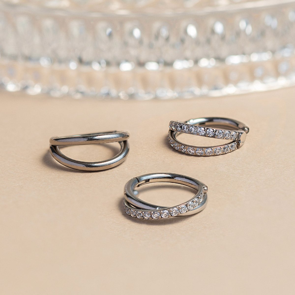 Three silver clicker hoops with double-bar and criss-cross pavé styles set with clear stones, on a cream surface