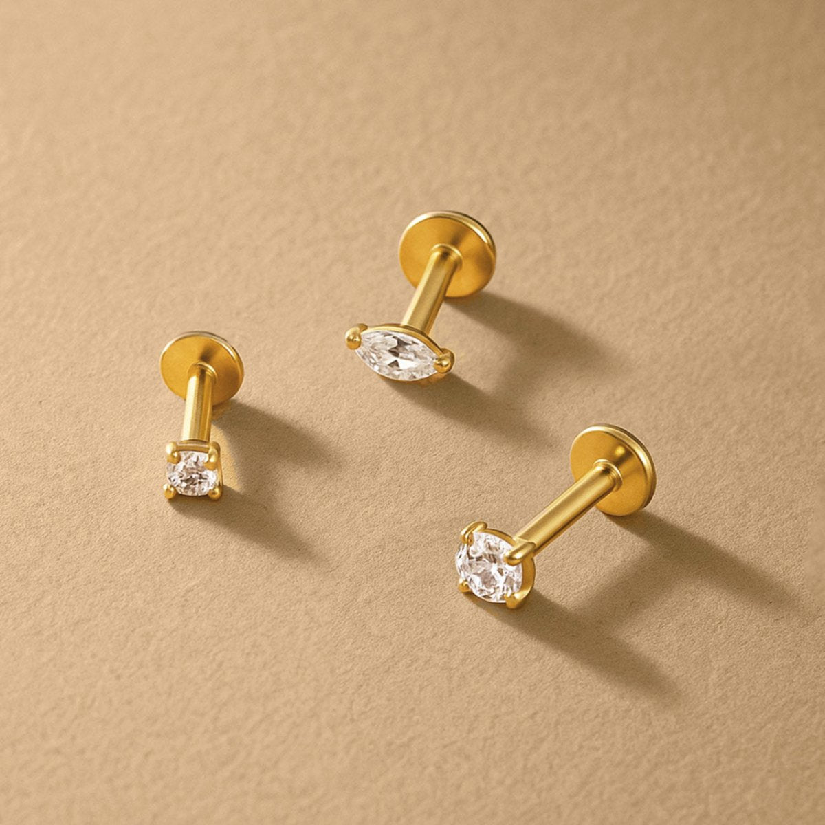 Three gold flat back studs with clear marquise and round stones, on a cream background | #Gemstone_White Zirconia