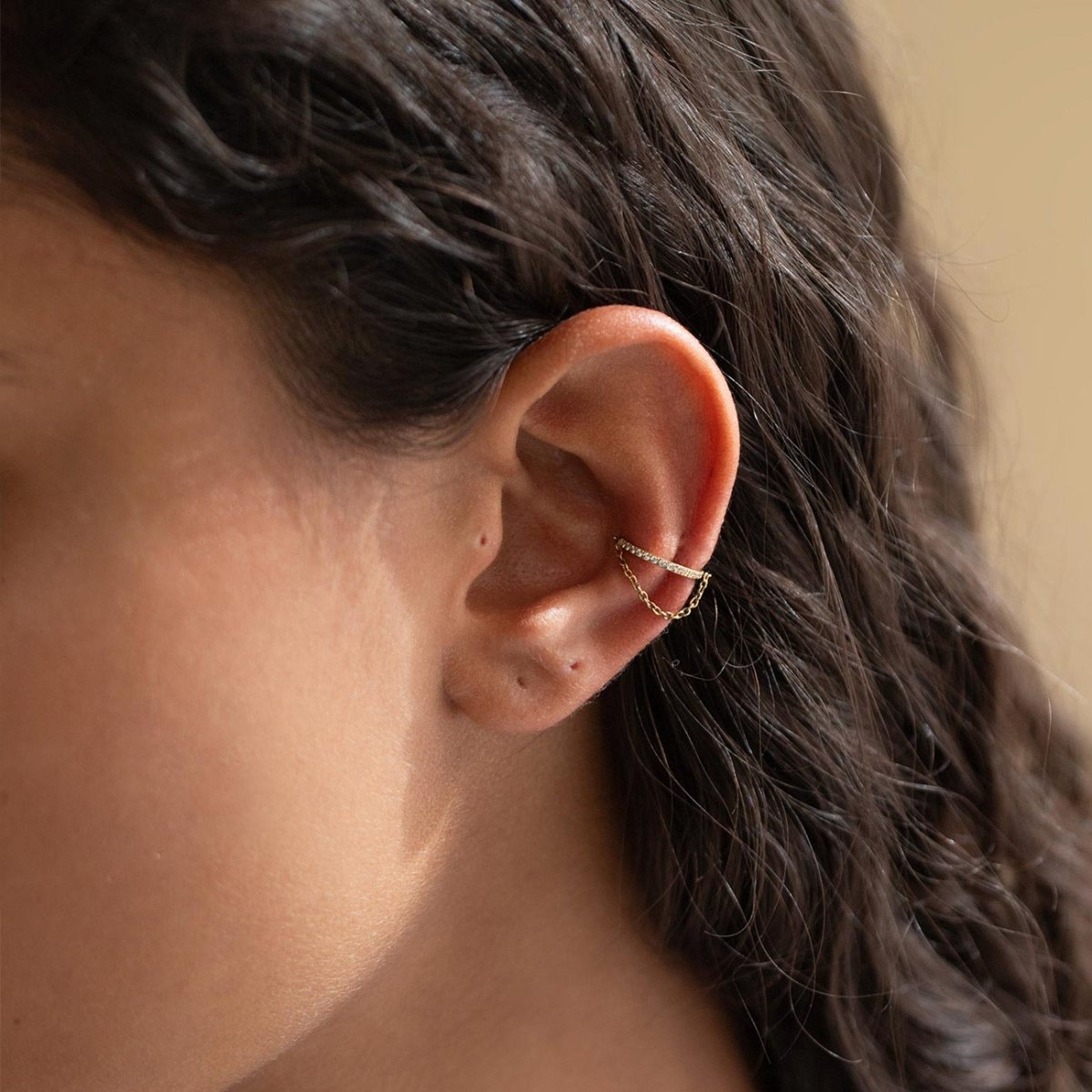 Gold titanium cartilage chain hoop with white stones, shown on a model's conch