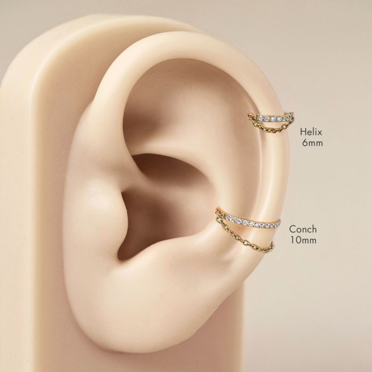 Gold titanium cartilage chain hoops with white stones on a placement guide, helix and conch