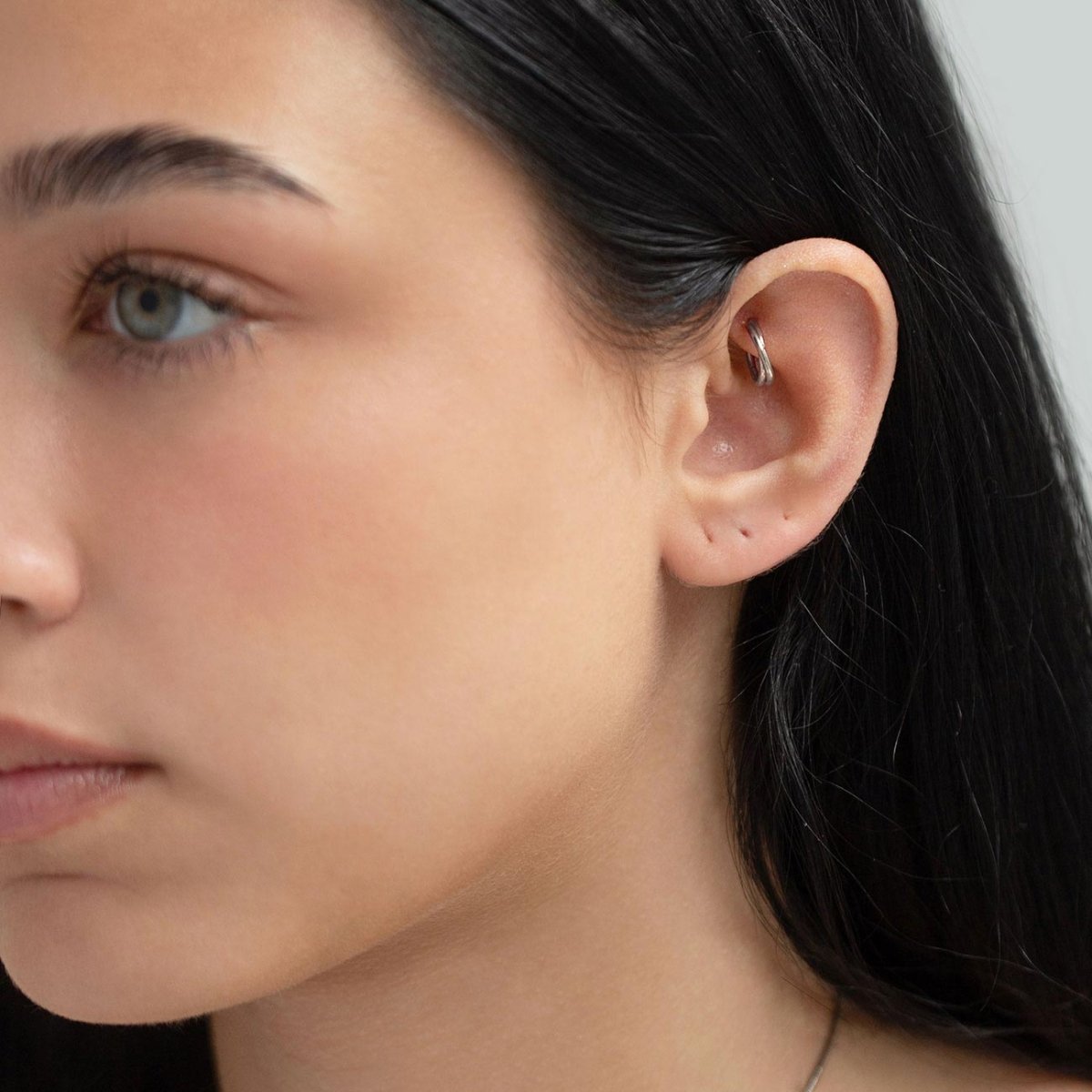 Silver titanium criss-cross cartilage hoop shown on a model's helix piercing