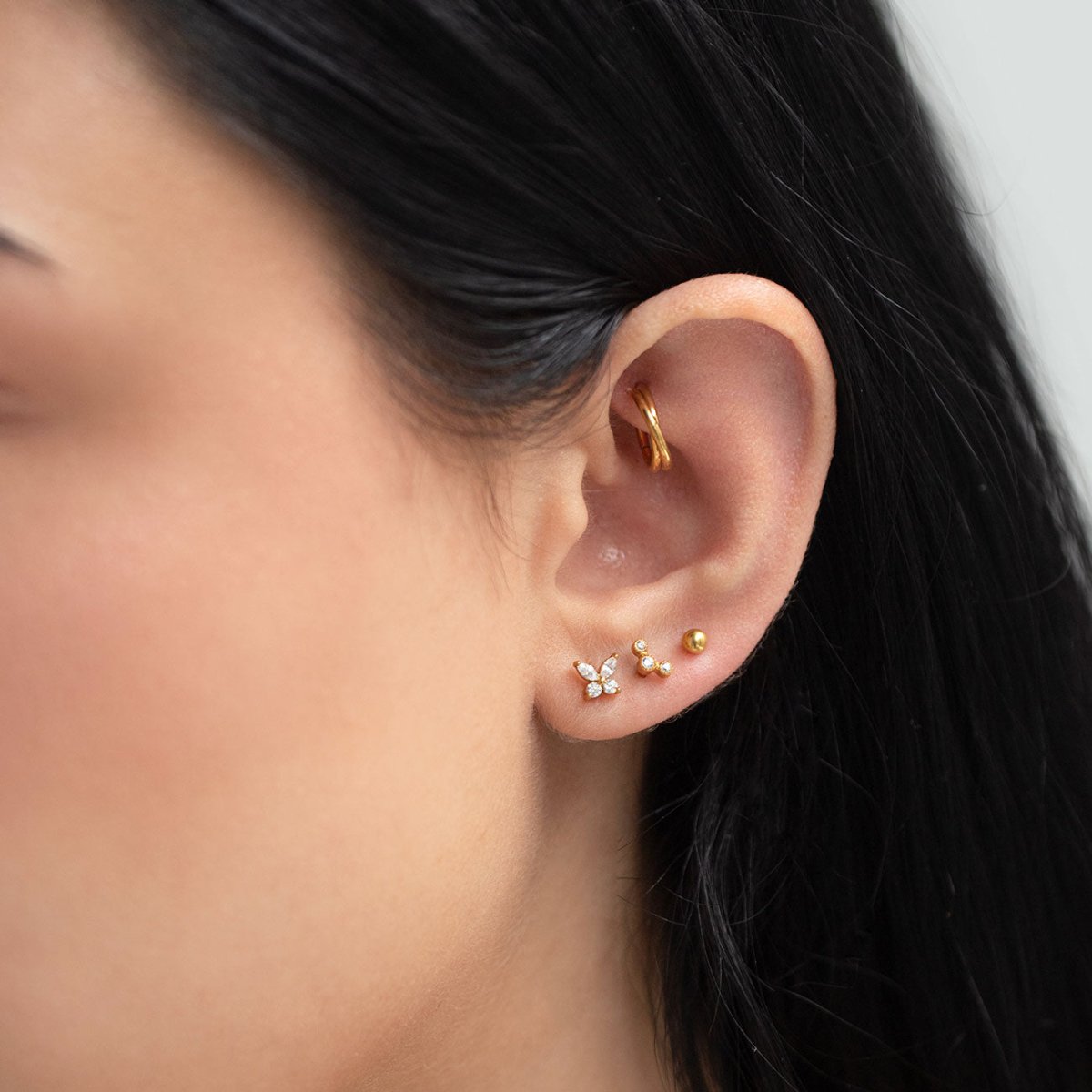 Gold titanium criss-cross cartilage hoop shown on a model's helix in an ear stack