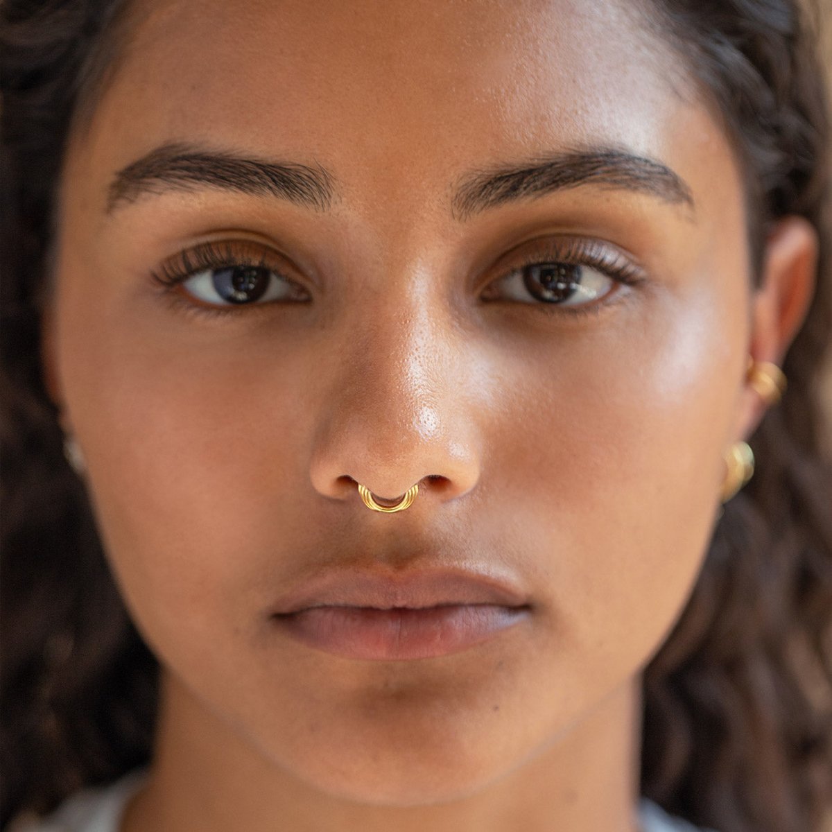 Gold titanium ridged hoop shown worn on a model's nose, front view