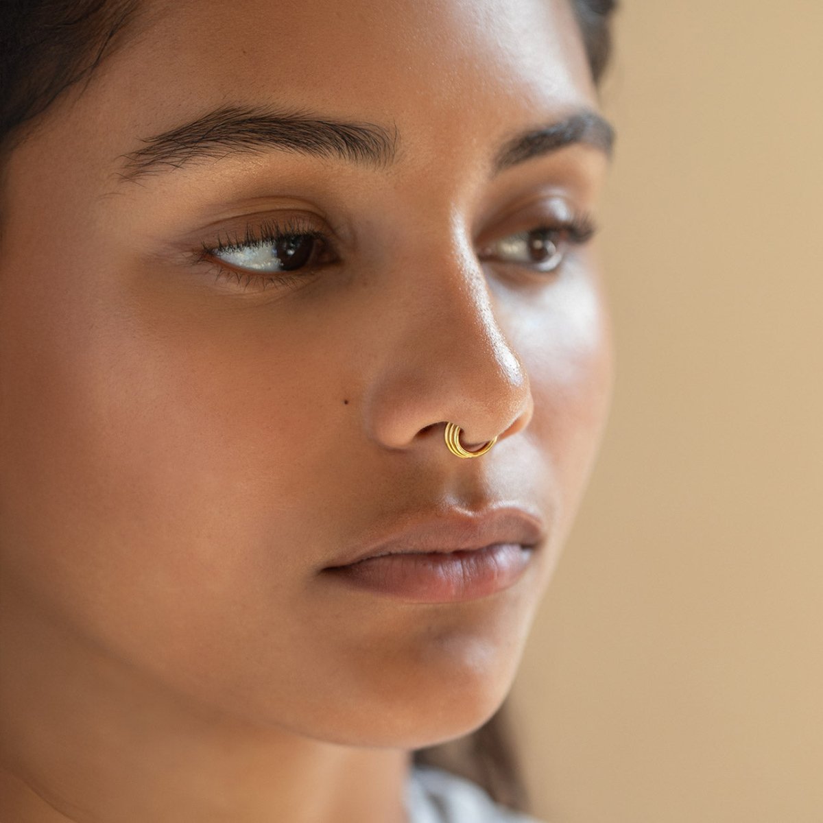 Gold titanium ridged hoop worn on a model's nose, close-up profile view