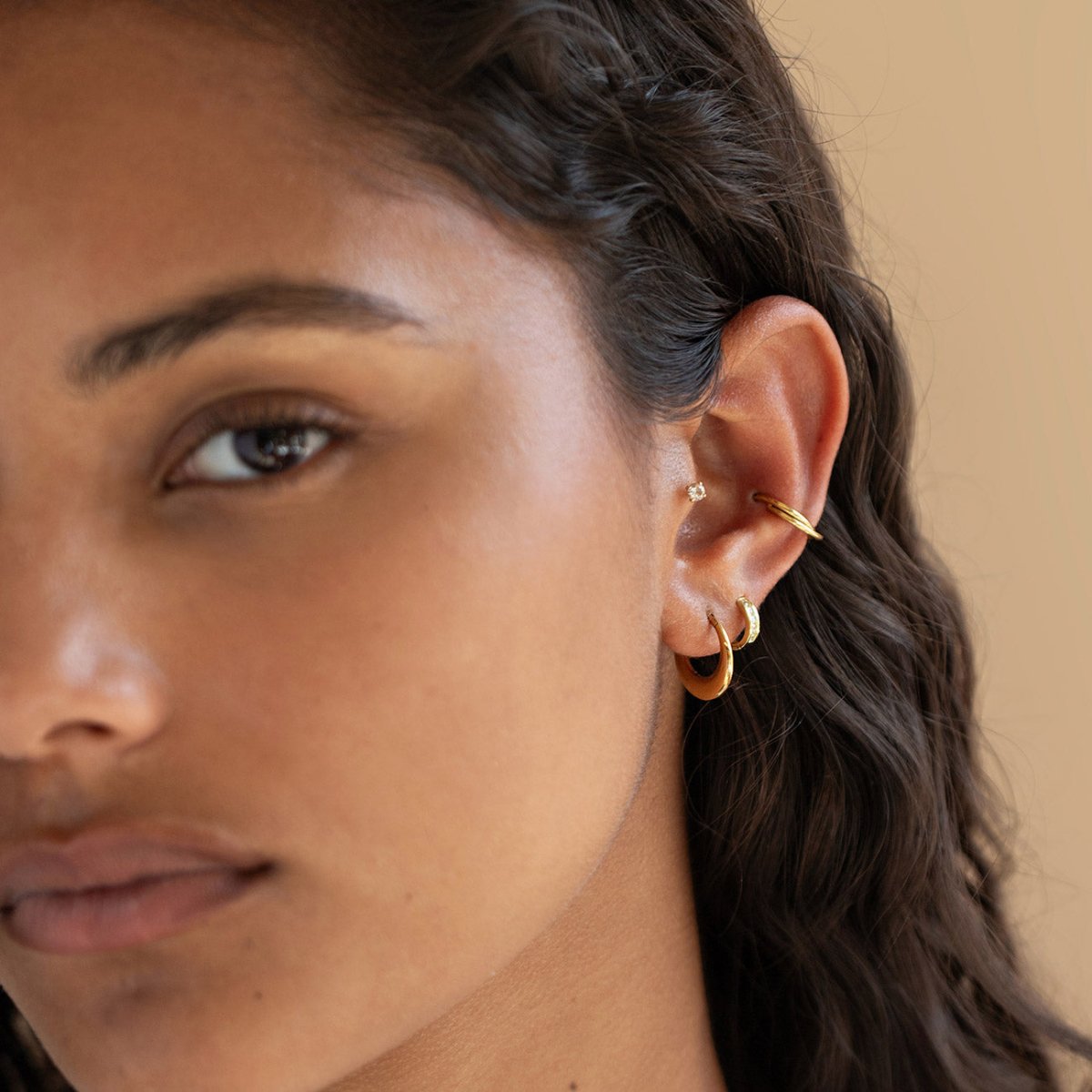 Gold titanium domed clicker hoop styled in a stack on a model's ear