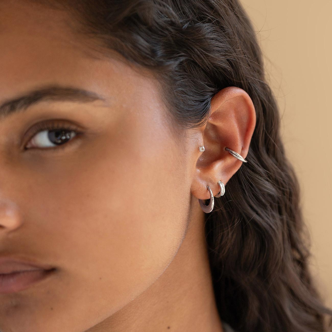 Silver titanium criss-cross cartilage hoop shown on a model's helix above lobe hoops