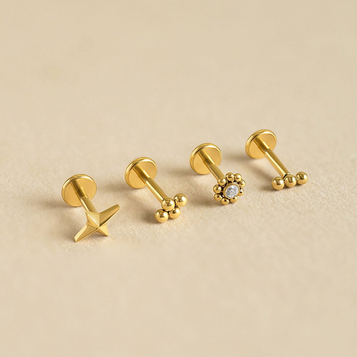 Four gold flat back studs in star, beaded, and clear-stone styles on a cream background