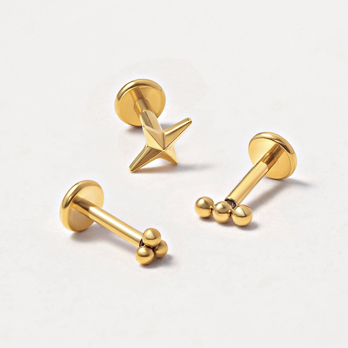 Close-up of three gold flat back studs in star and beaded styles on a light surface