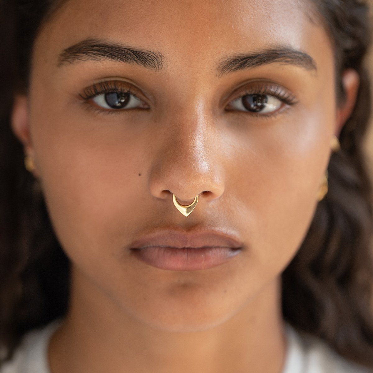 Gold titanium clicker hoops including a V-shape shield and clear crystal styles, on a cream background