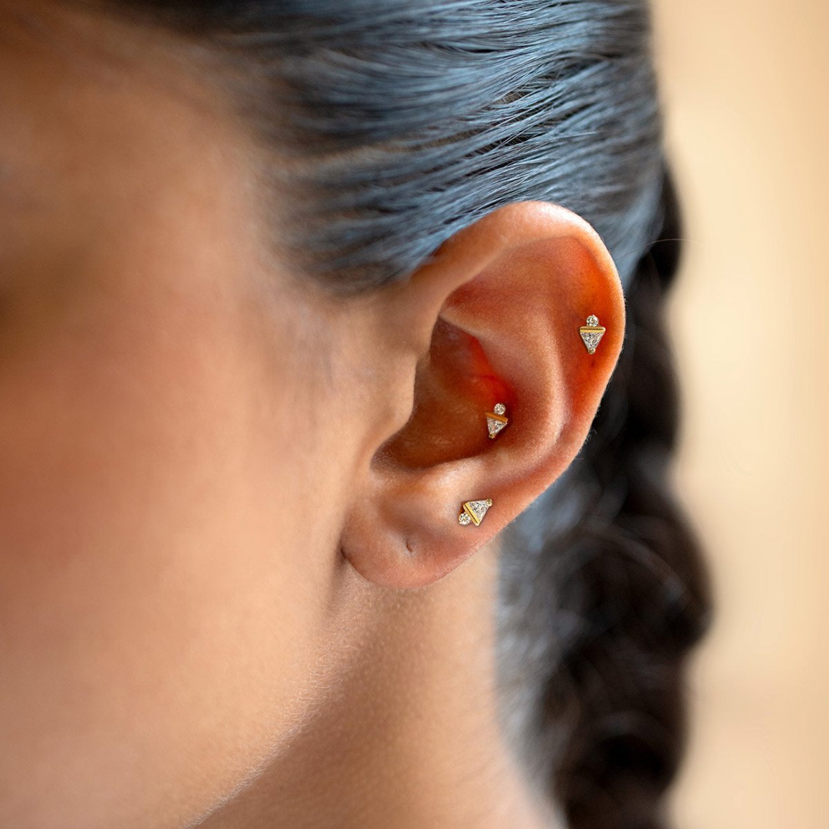 Gold Titanium flat back stud earrings with triangle-shaped and round crystals, shown on a model's ear.