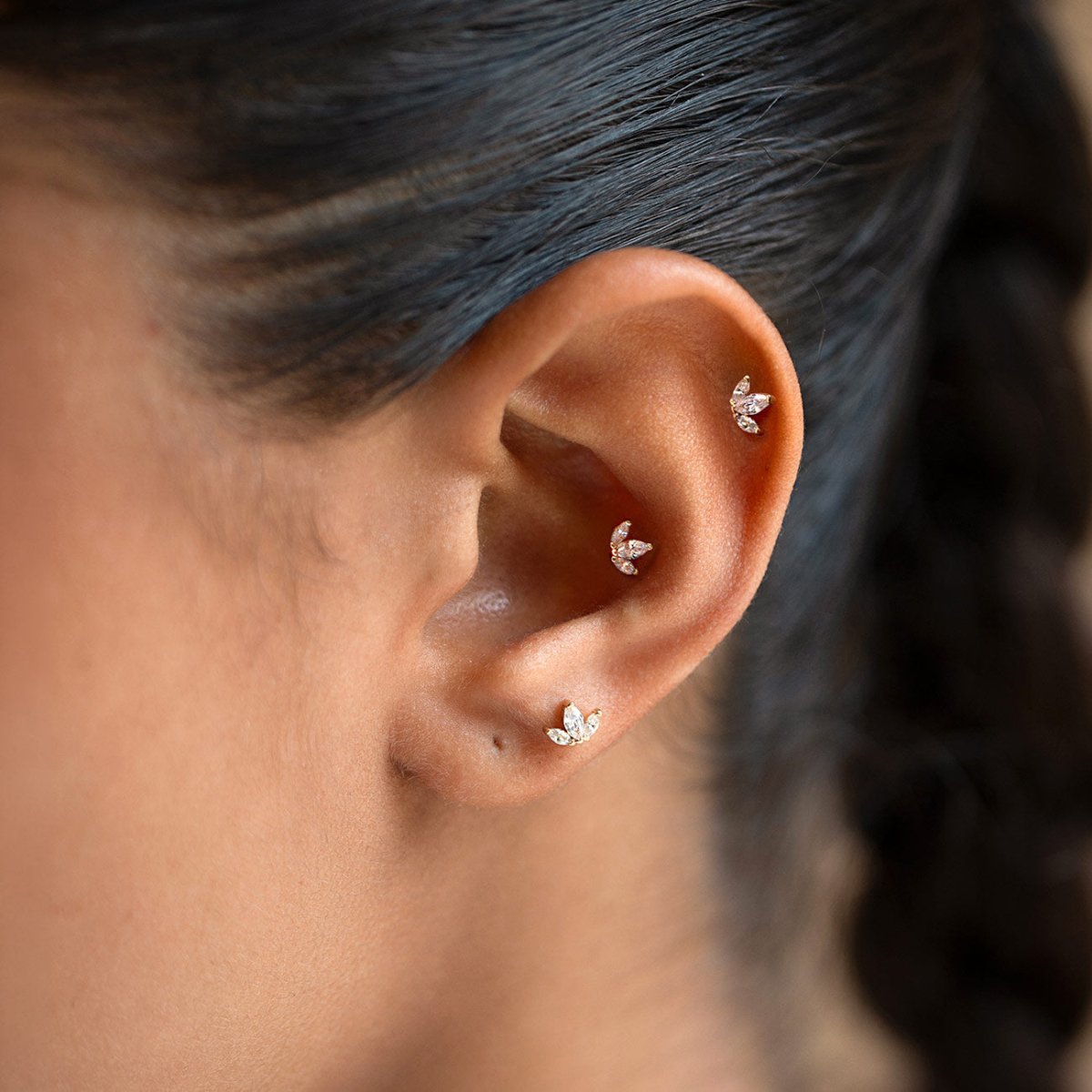 14K gold flat back stud earrings with three marquise-shaped crystals, shown on a model's ear.