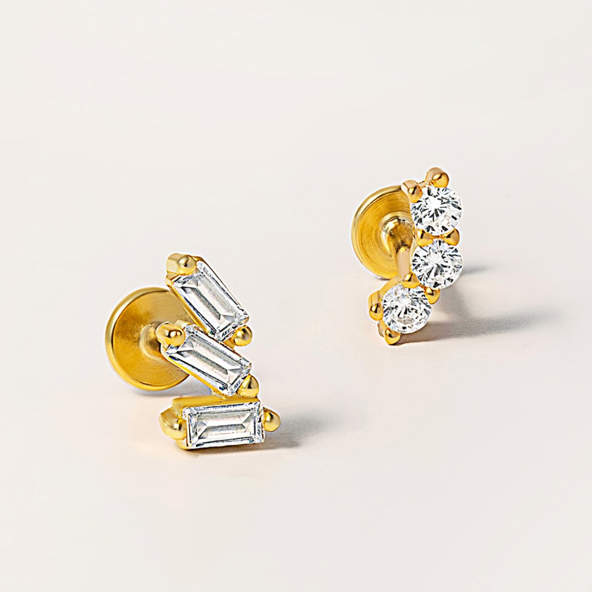 Gold flat back studs with baguette and round clear stones, close-up on a cream background