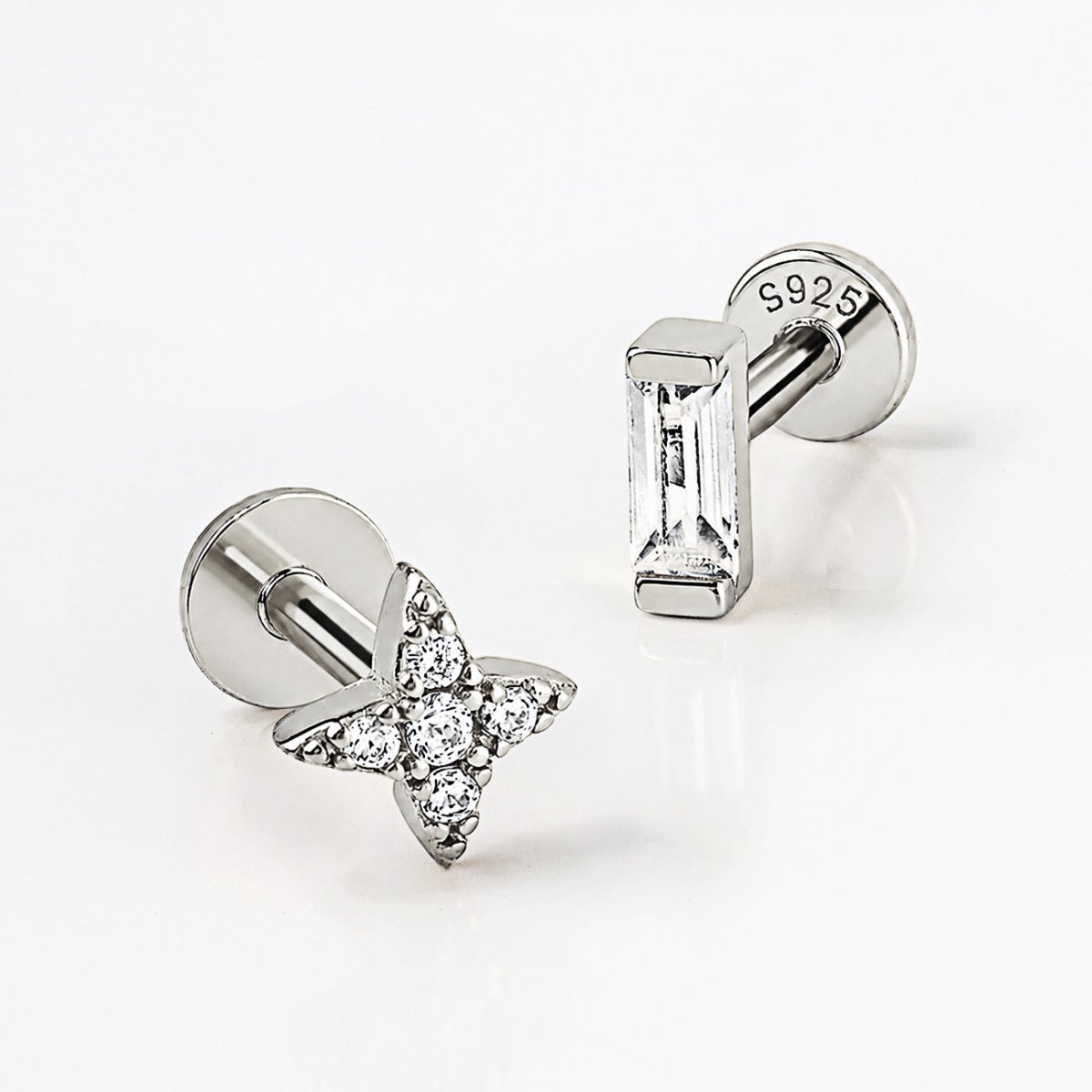 Two silver flat back studs on a white surface, one baguette crystal and one crystal-set star flare