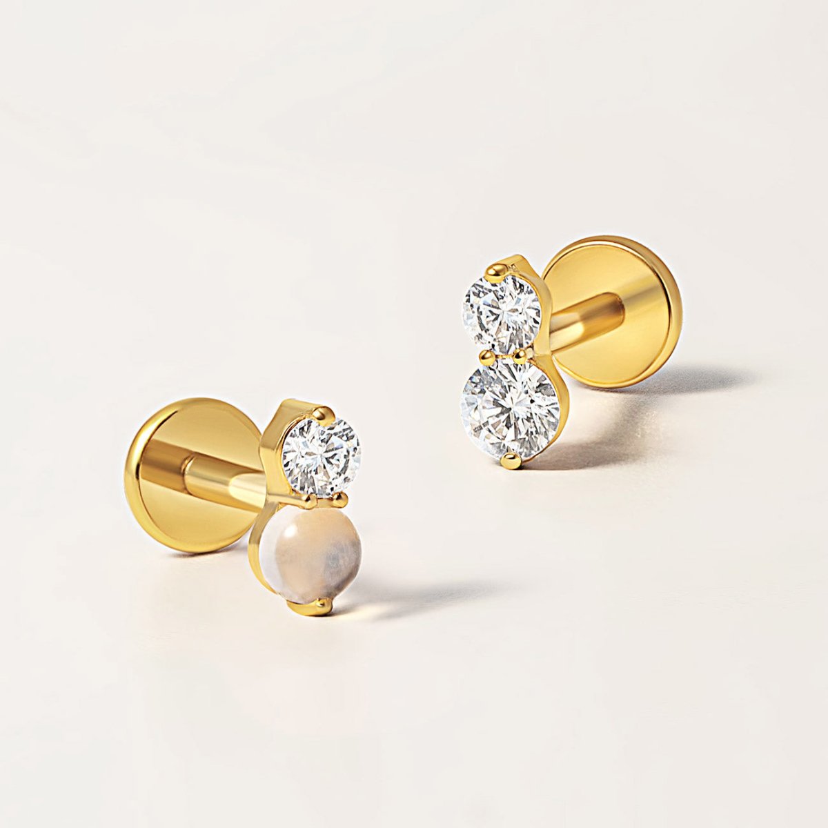 Gold titanium flatback studs with a clear stone and a white stone, close-up detail on a cream background | #Gemstone_White Opal