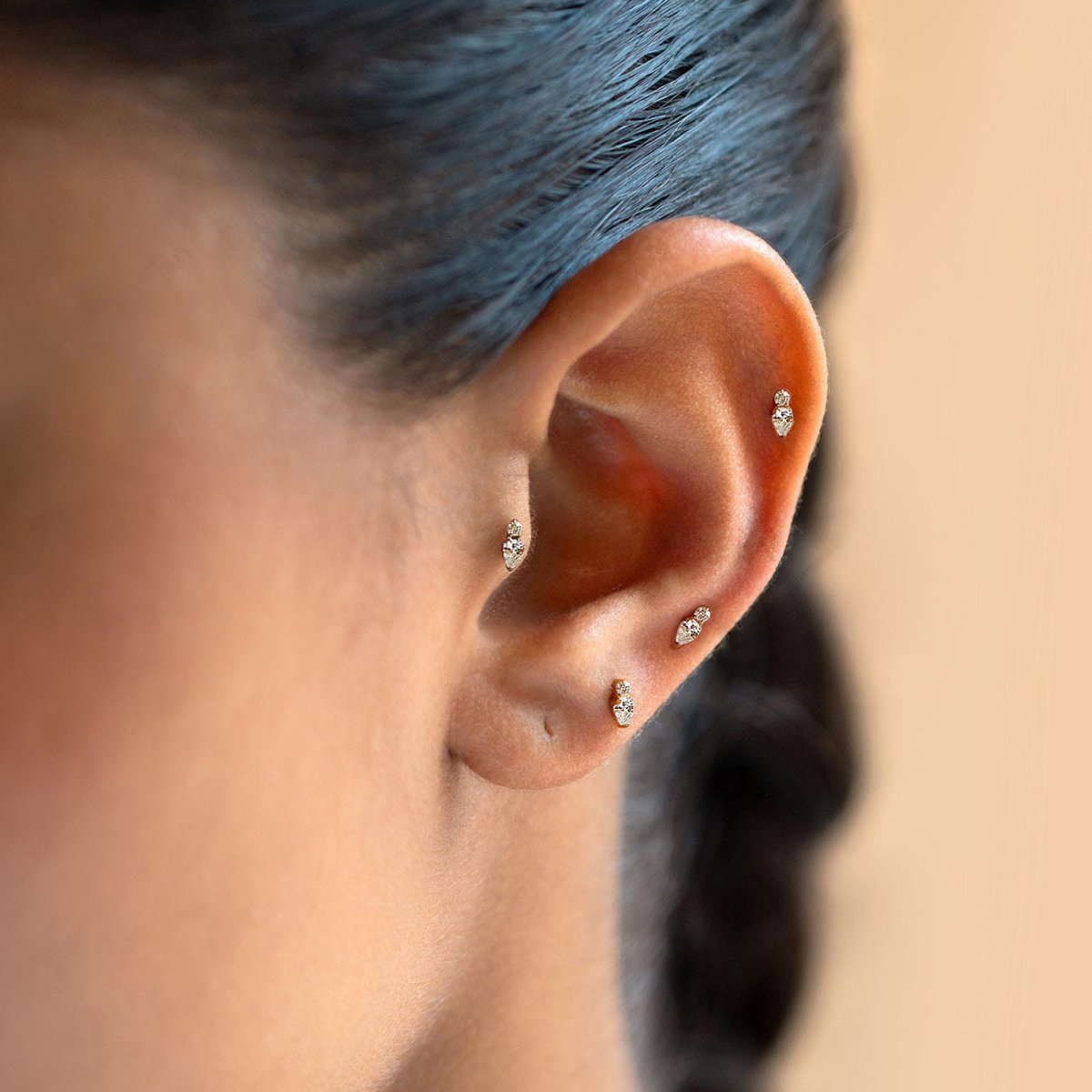 Gold flat back stud earrings with a round crystal and pear-shaped crystal, shown on a model's ear. | #Gemstone_White Zirconia
