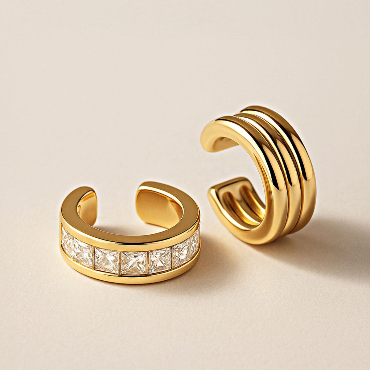 Gold ridged ear cuff beside a square clear-stone band ear cuff, on a cream background