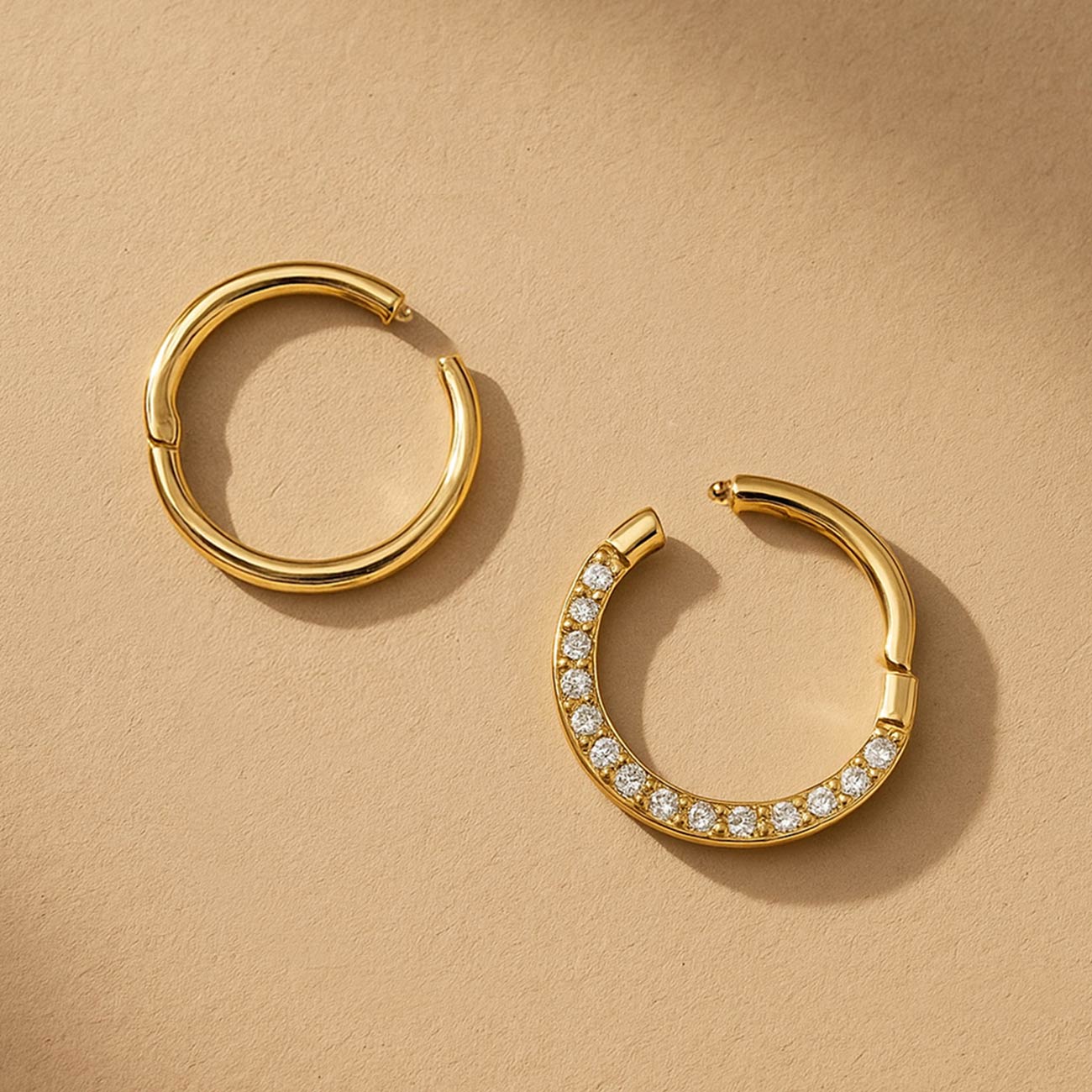 Two gold seamless clicker hoops, one plain and one pavé with clear stones, on a cream background