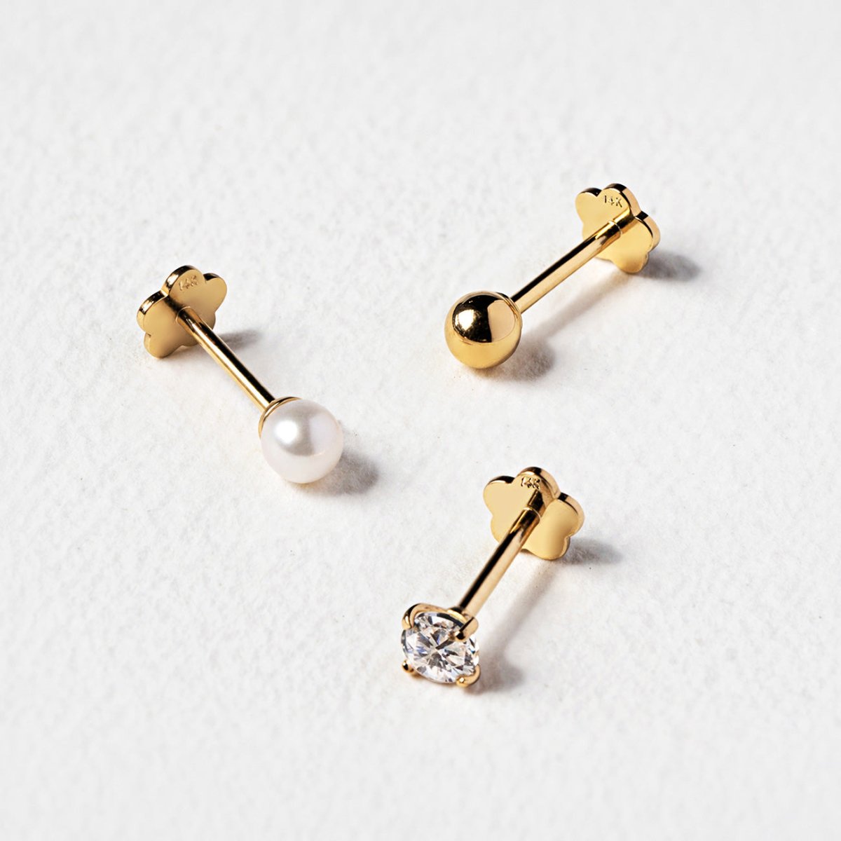Close-up detail of 14K gold flat back studs with a clear stone, a pearl and a plain ball