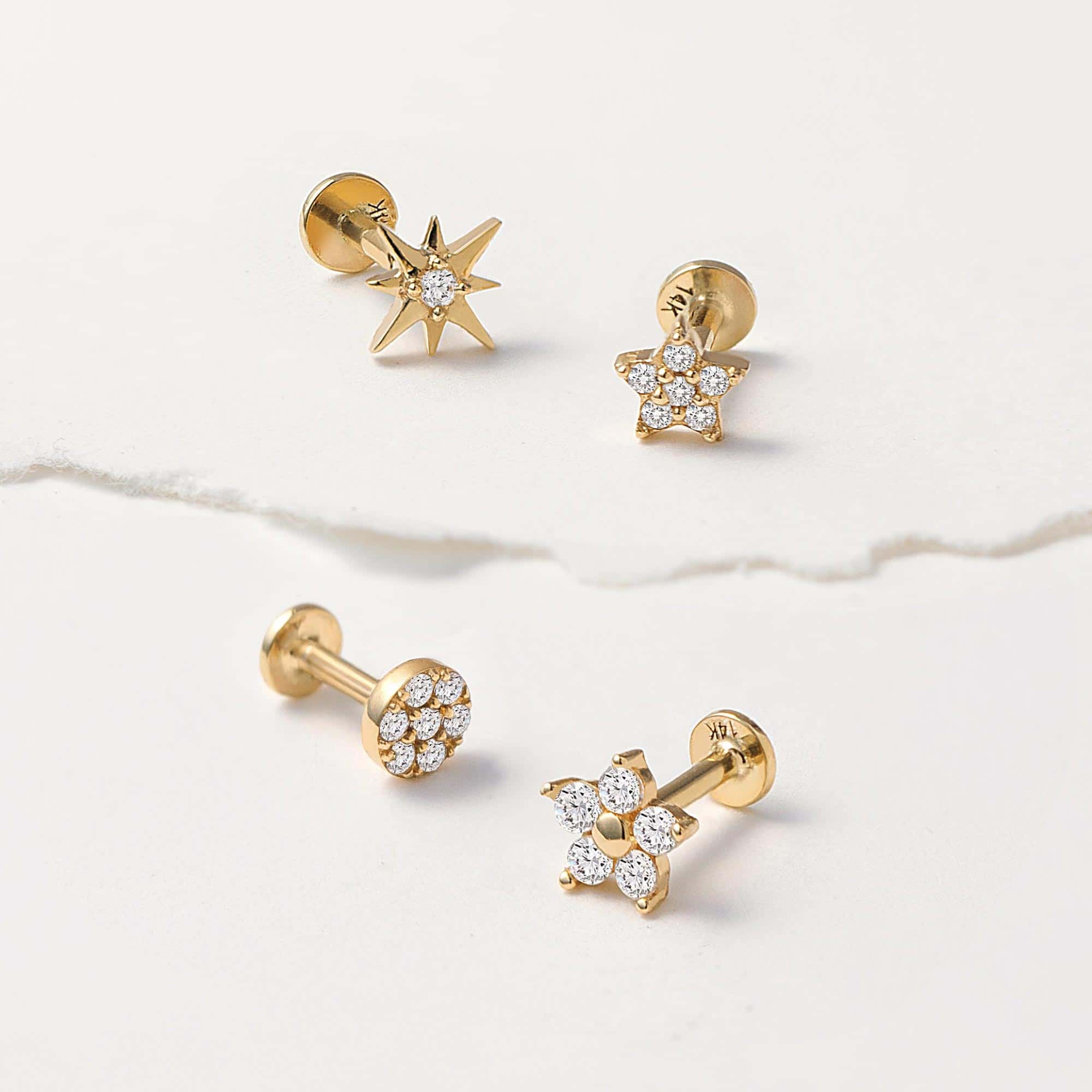 14K gold pavé star and starburst flat back studs with white zirconia, on cream marble