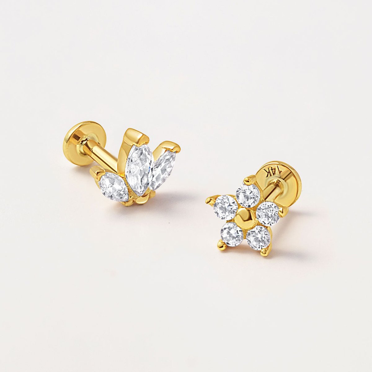 Two gold flat back studs with clear stones in marquise cluster and flower shapes, on a white background