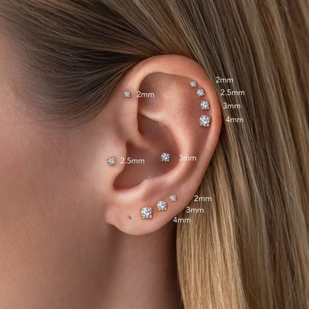 14K gold round stud earrings shown on a model's ear with 2mm, 2.5mm, 3mm, and 4mm size comparisons. 
