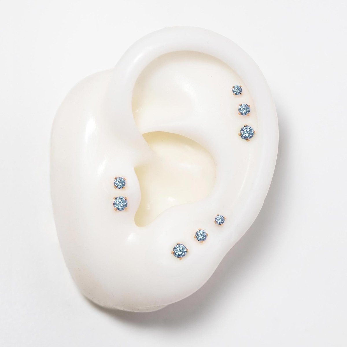 14K gold flat back aquamarine studs in three sizes on a silicone ear, pale blue stones