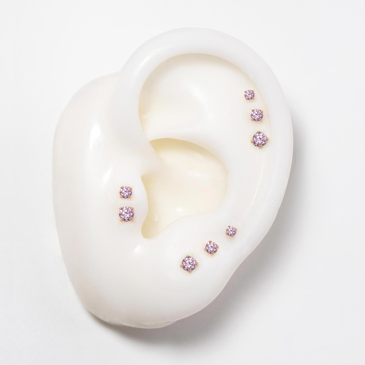14K gold flat back pink sapphire studs in three sizes on a silicone ear, soft pink stones