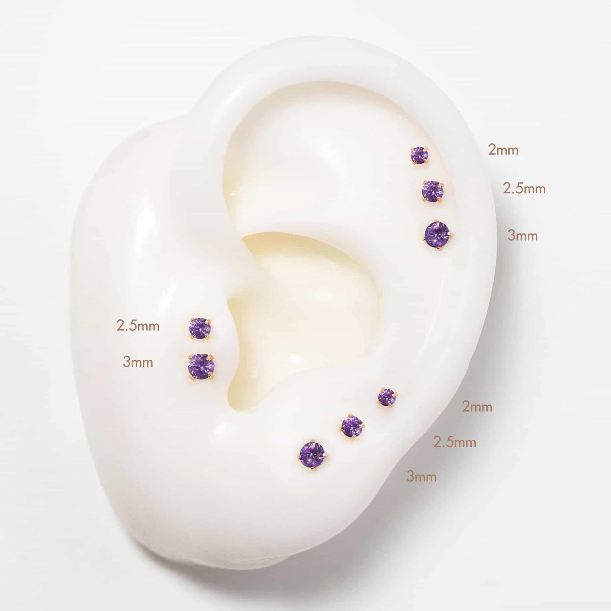 14K gold flat back amethyst studs in 2mm, 2.5mm and 3mm sizes on a silicone ear, purple stones