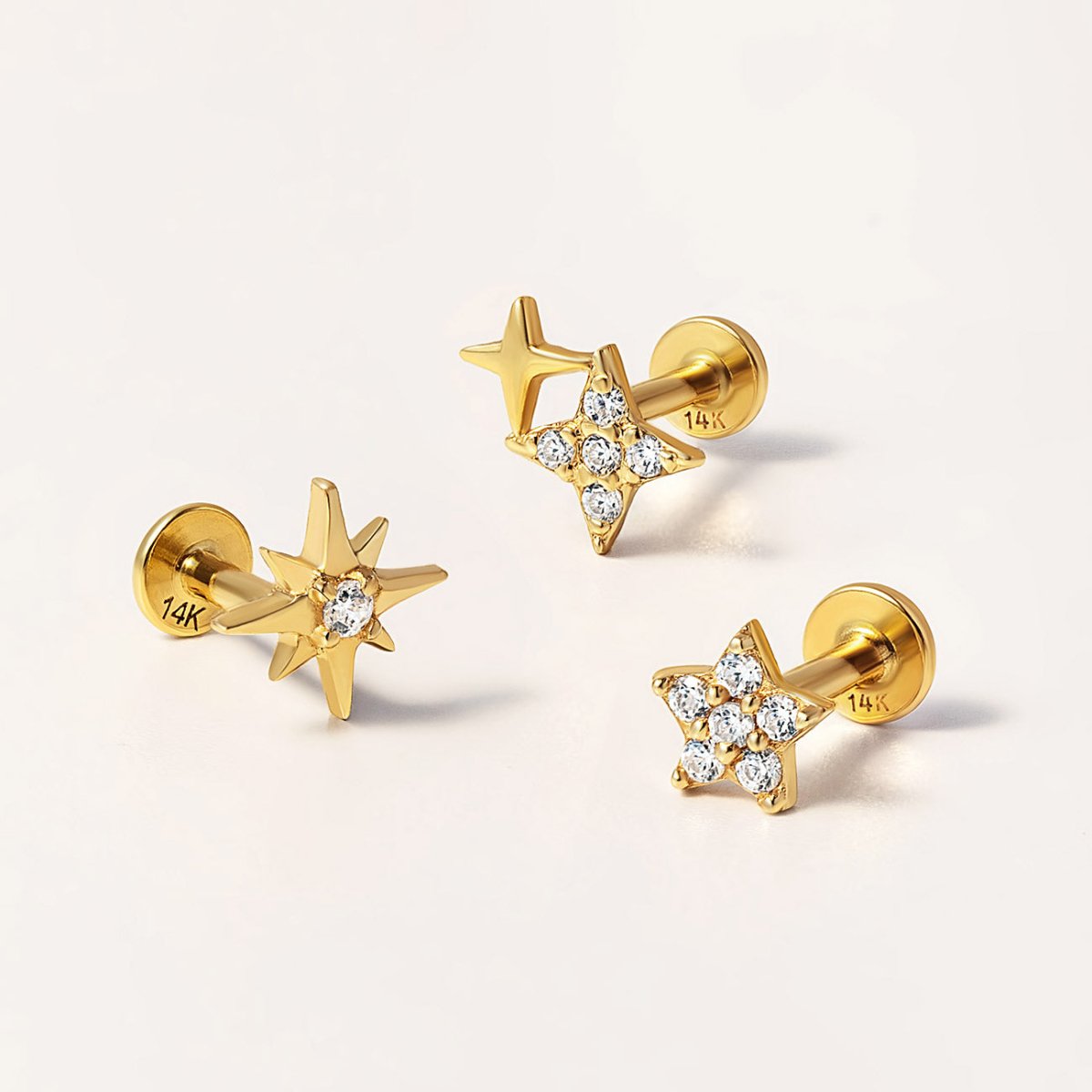 Three gold star and starburst flat back studs with clear stones, on a cream background