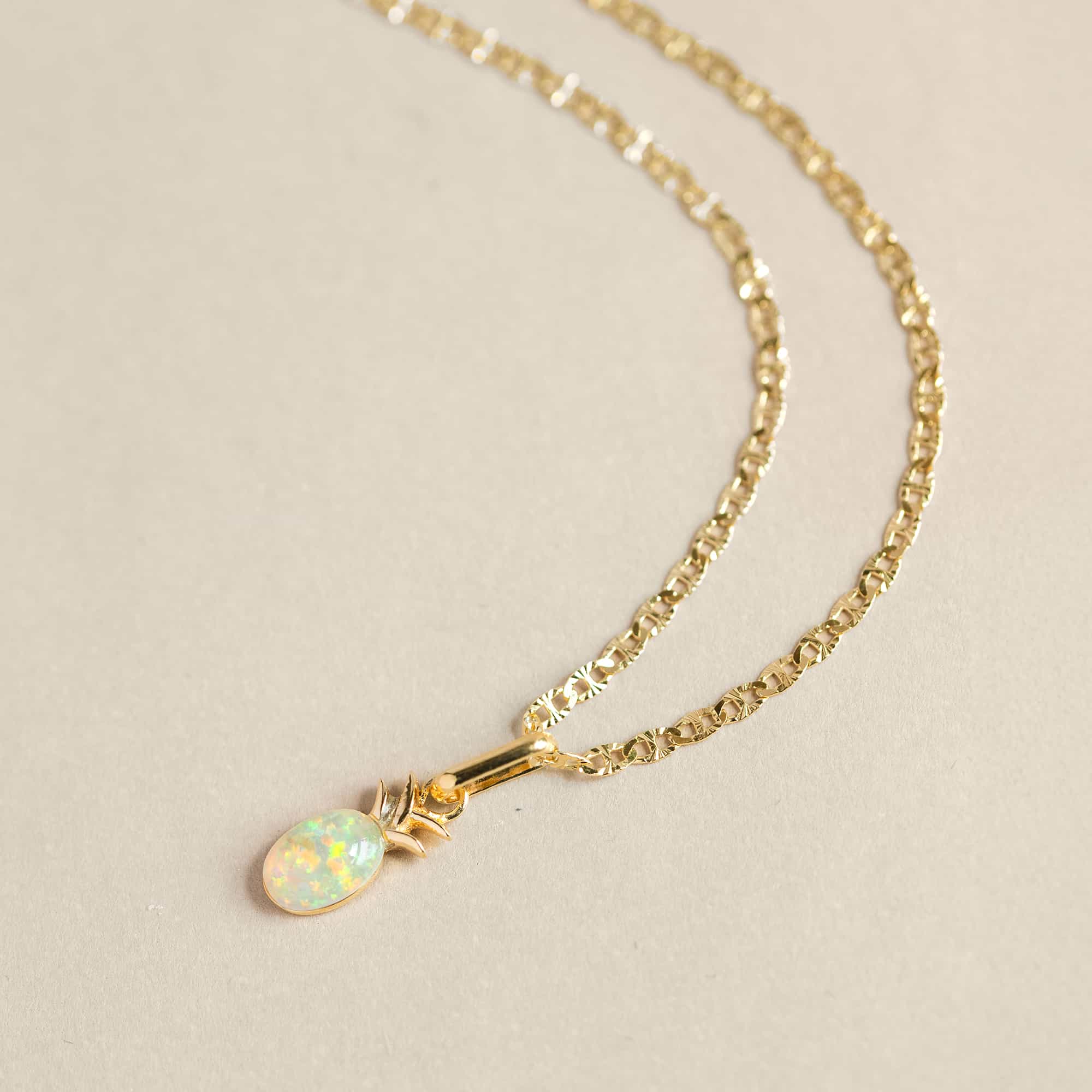 Gold mariner chain with an oval opal pineapple pendant, on a cream background