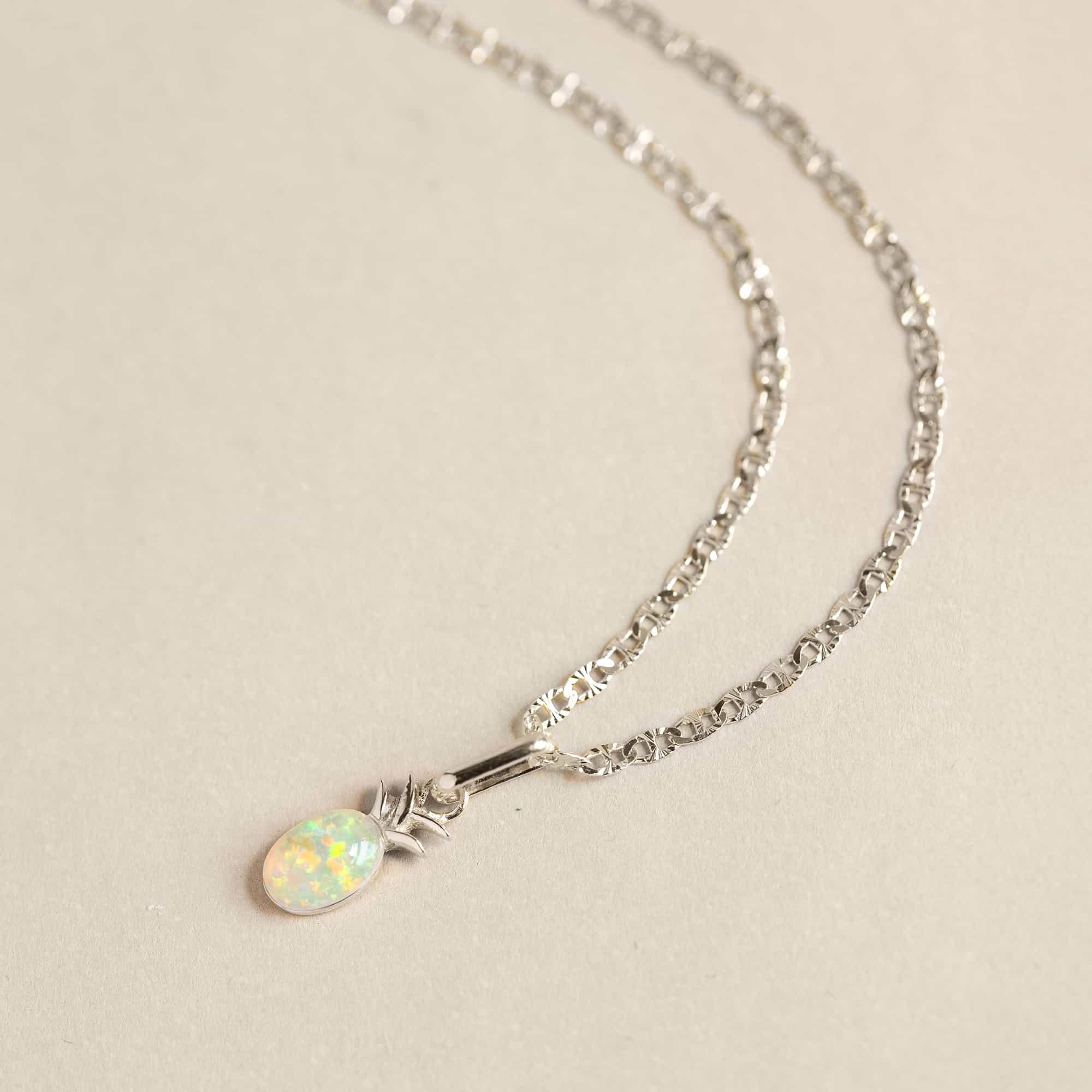 Silver mariner chain with an oval opal pineapple pendant, on a cream background