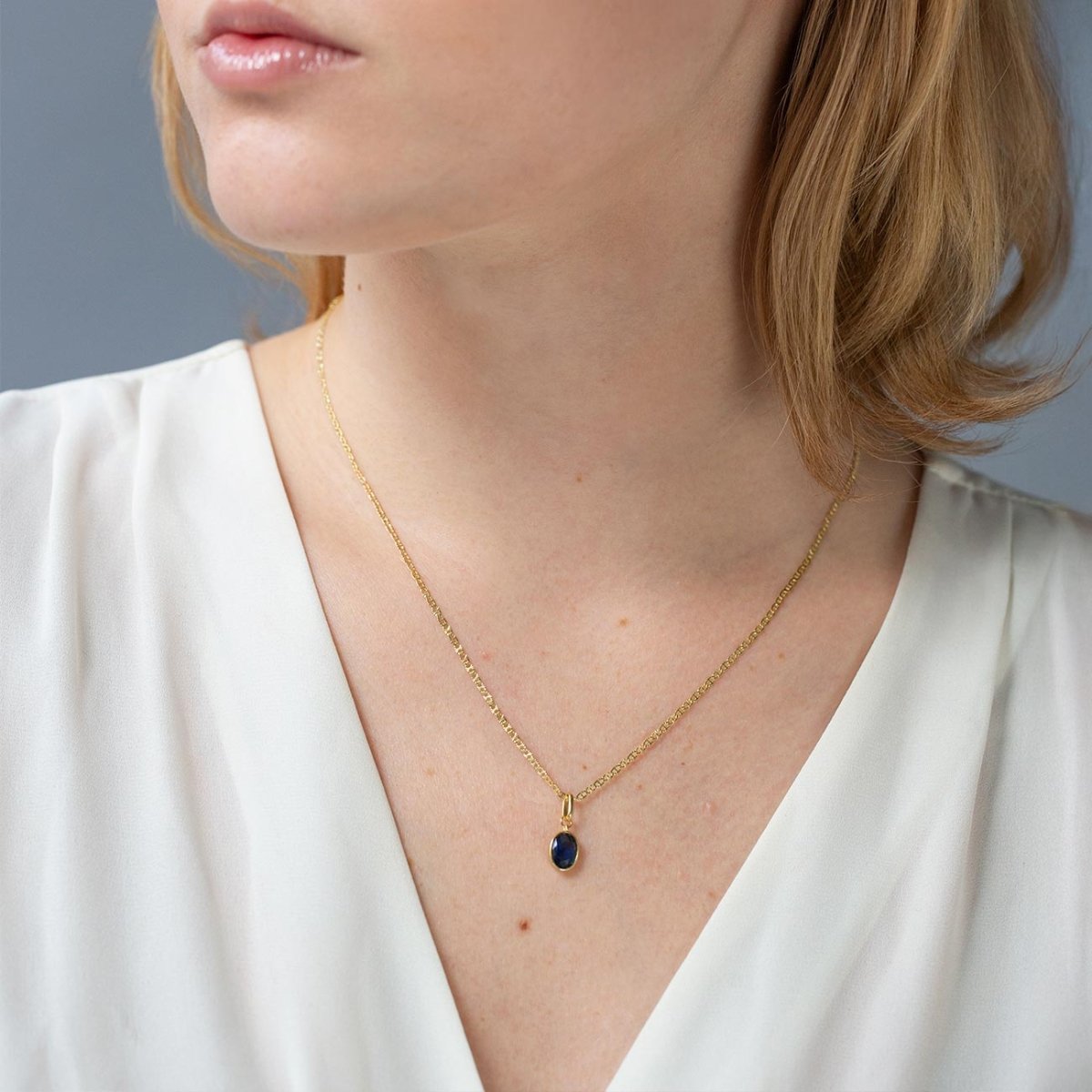 Gold vermeil oval blue sapphire charm pendant on a chain, shown on a model's neckline