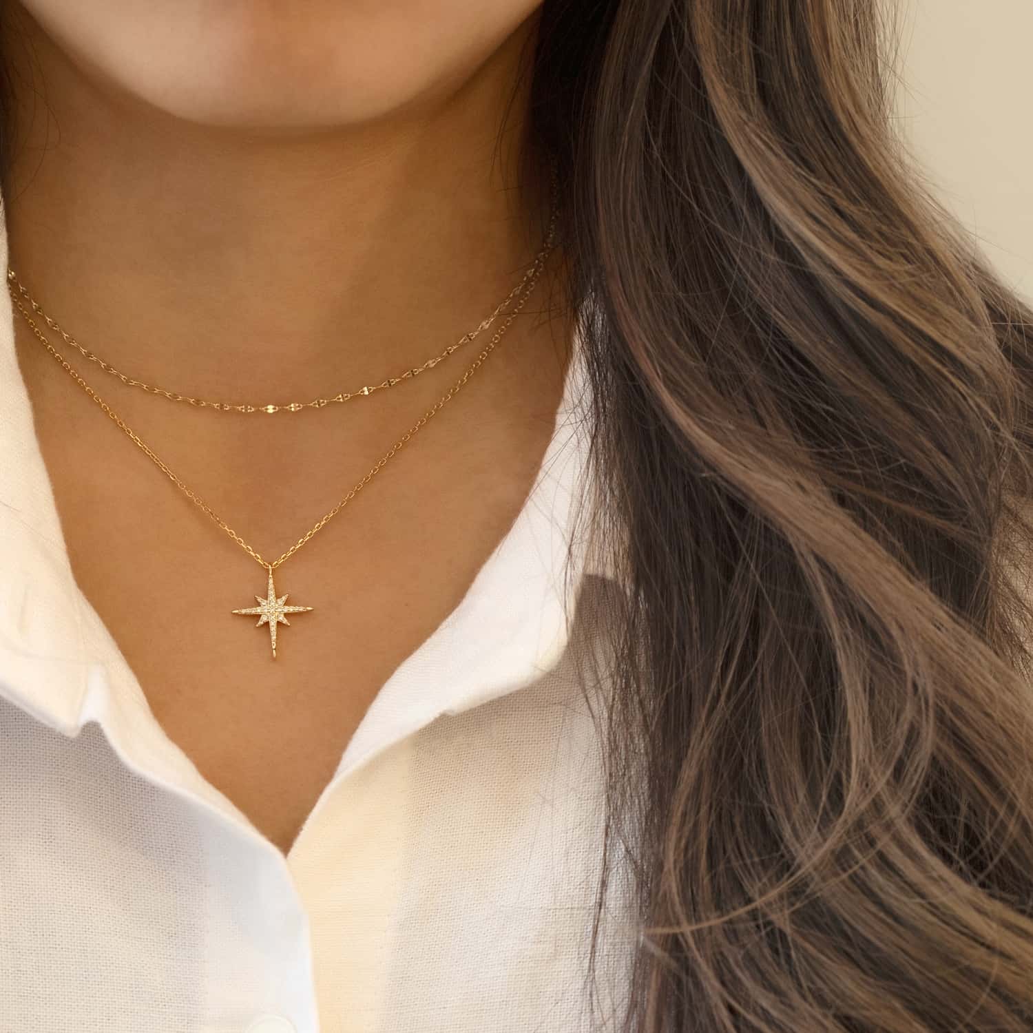 Gold vermeil starburst pendant with clear stones, layered necklaces shown on a model in a white shirt