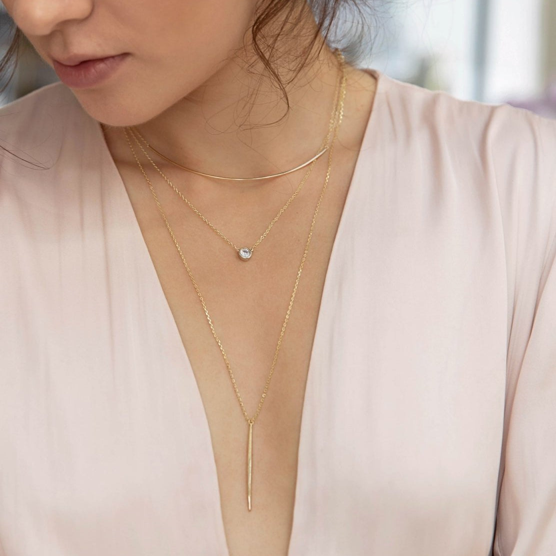 Gold vermeil curved bar necklace layered with a lariat drop, shown on a model's neckline