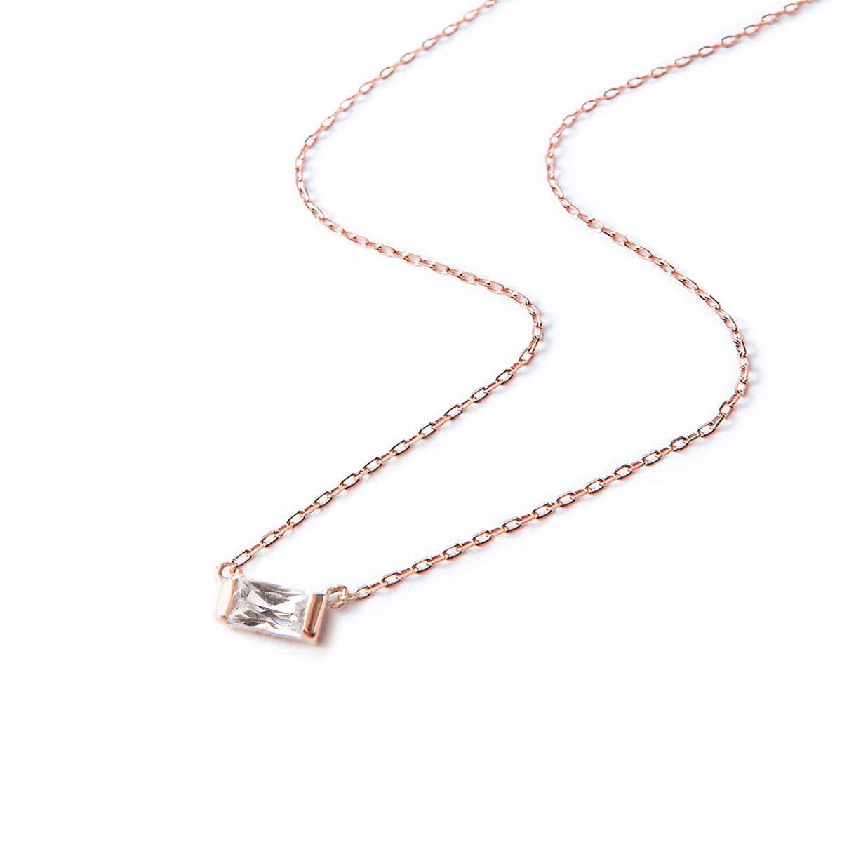Rose gold vermeil baguette necklace with a clear white zirconia pendant, laid on a white background