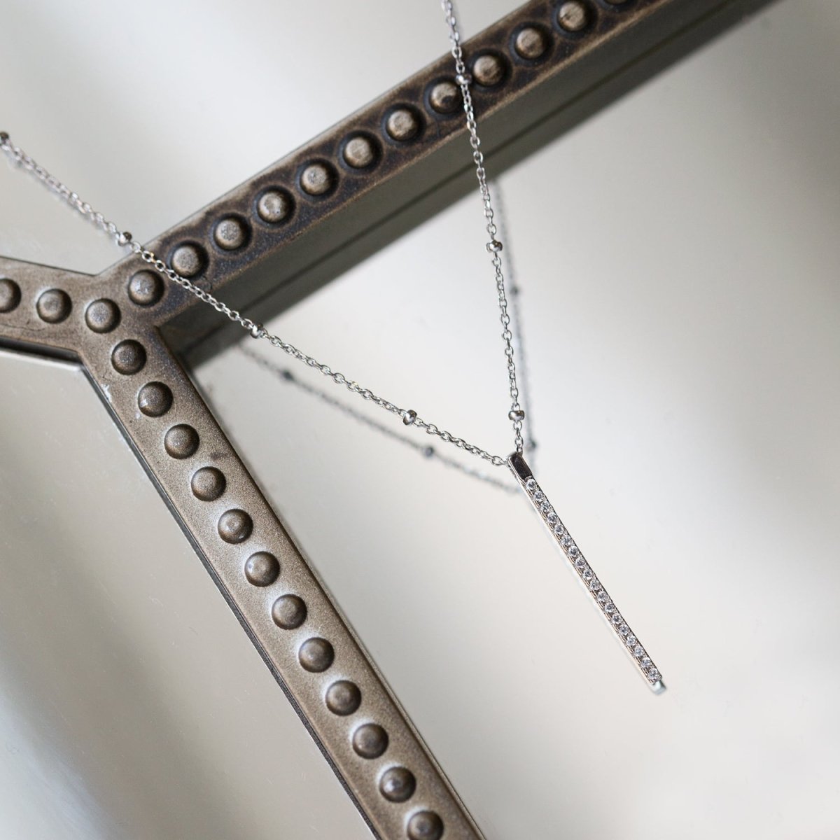 Sterling silver pavé bar pendant on a beaded chain, draped over a studded metal frame