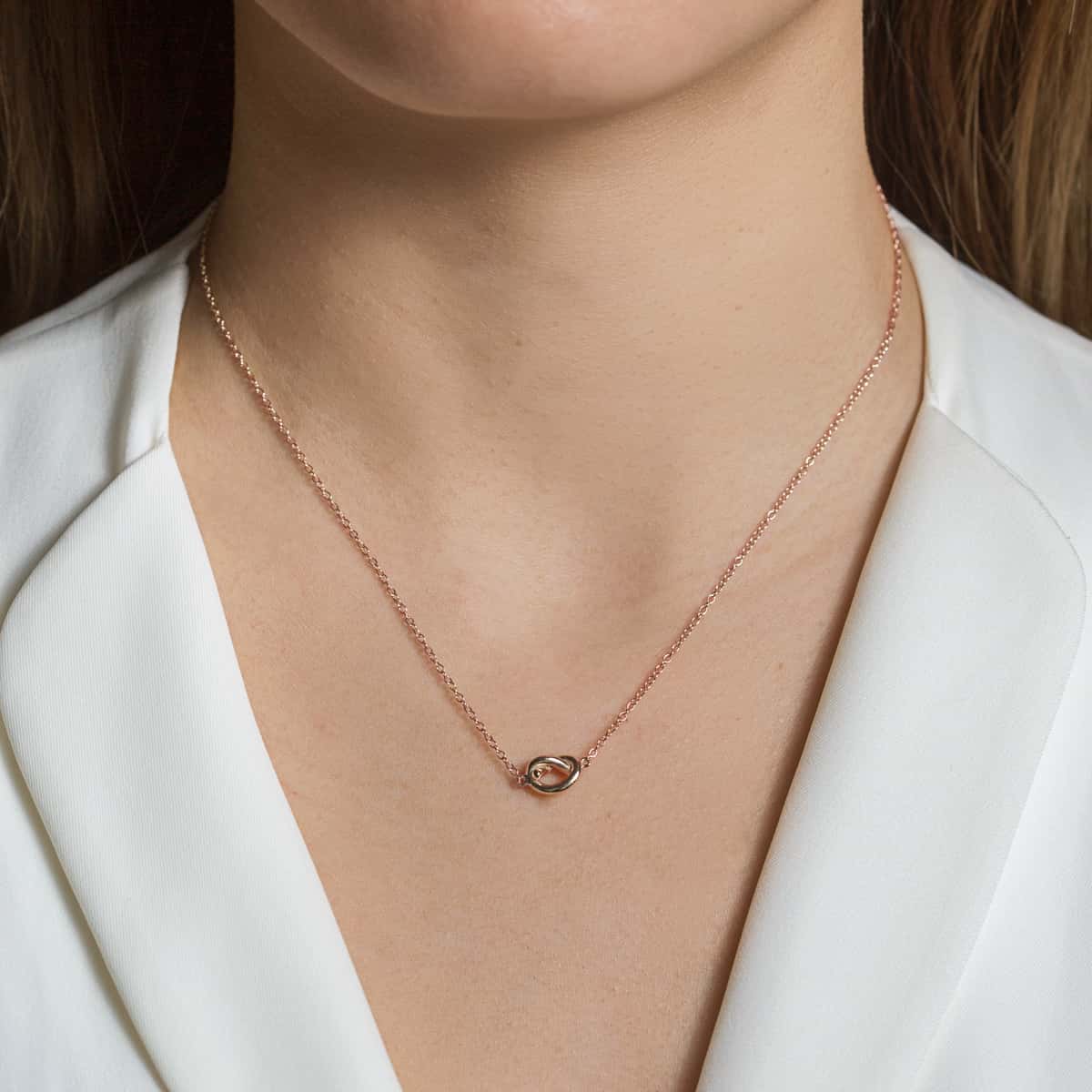 Rose gold vermeil love knot necklace with a small interlocking knot, shown on a model's neckline