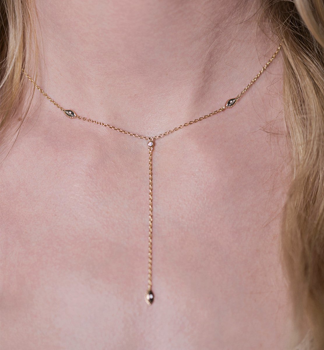 Gold vermeil evil eye lariat necklace with clear stones, shown on a model's neckline