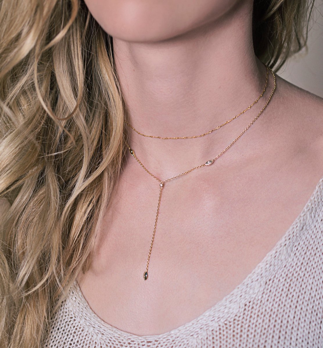 Gold vermeil evil eye lariat necklace layered with a chain, shown on a model's neckline