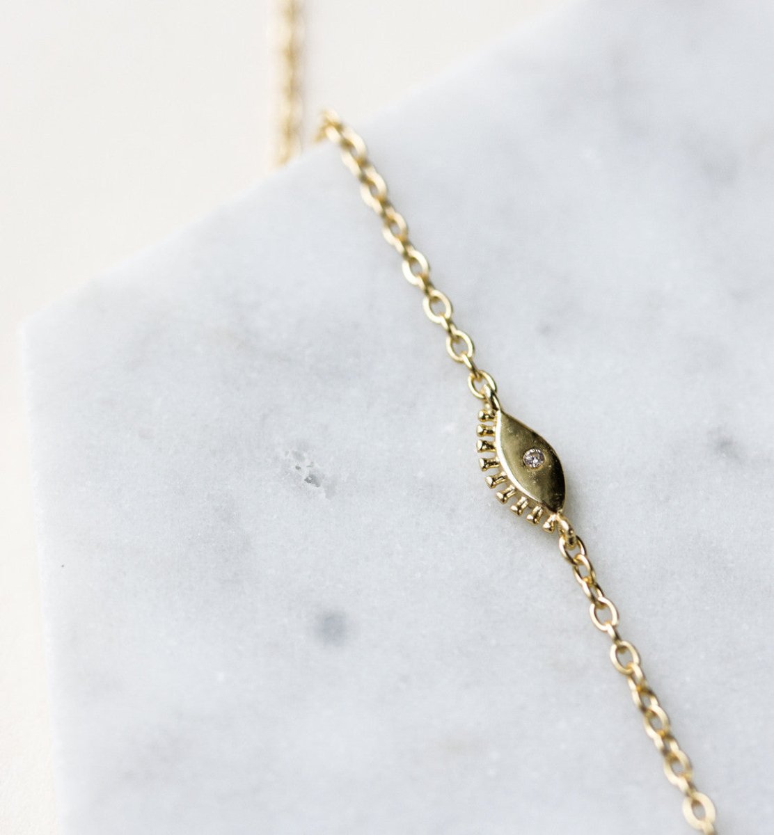 Gold vermeil lariat necklace, close-up detail of a marquise evil eye charm with a clear stone, on white marble
