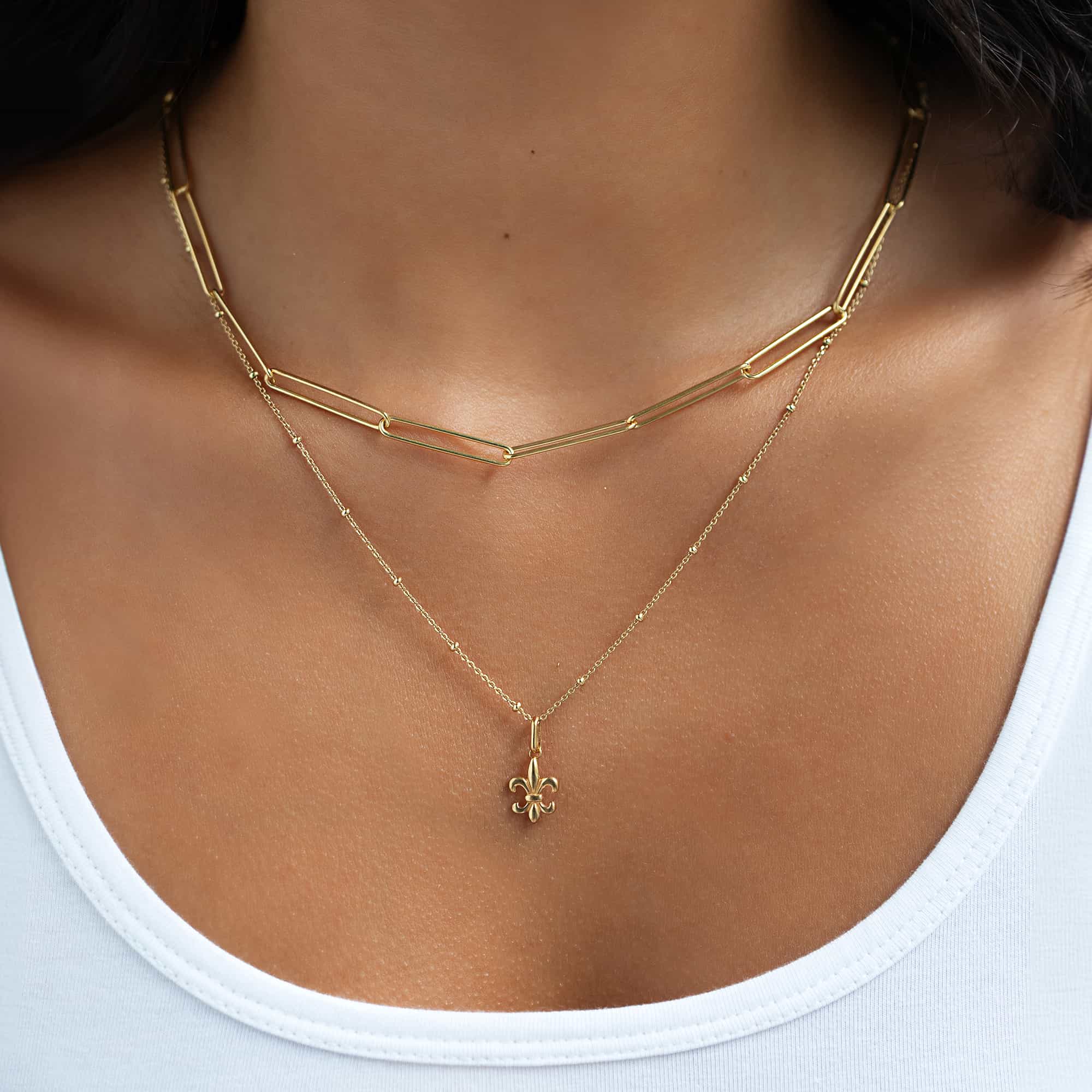 Gold vermeil fleur-de-lis pendant on a beaded chain, shown on a model's neckline