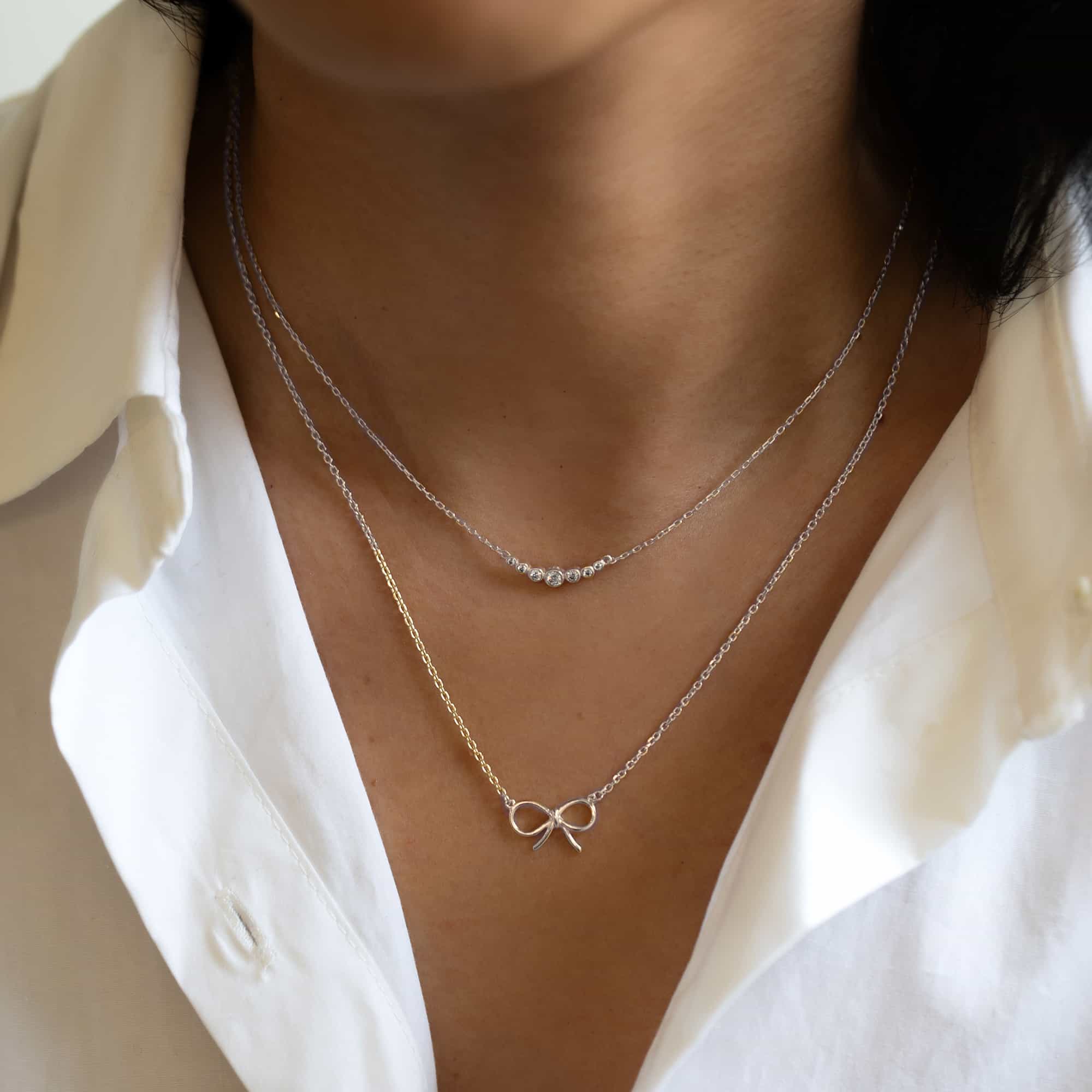Sterling silver curved bar necklace with graduated clear stones, shown layered on a model's neckline