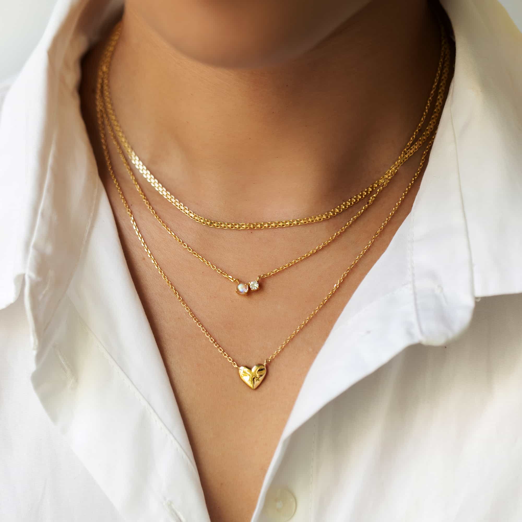 Three gold necklaces layered on a model's neckline, including a two-stone and a heart pendant