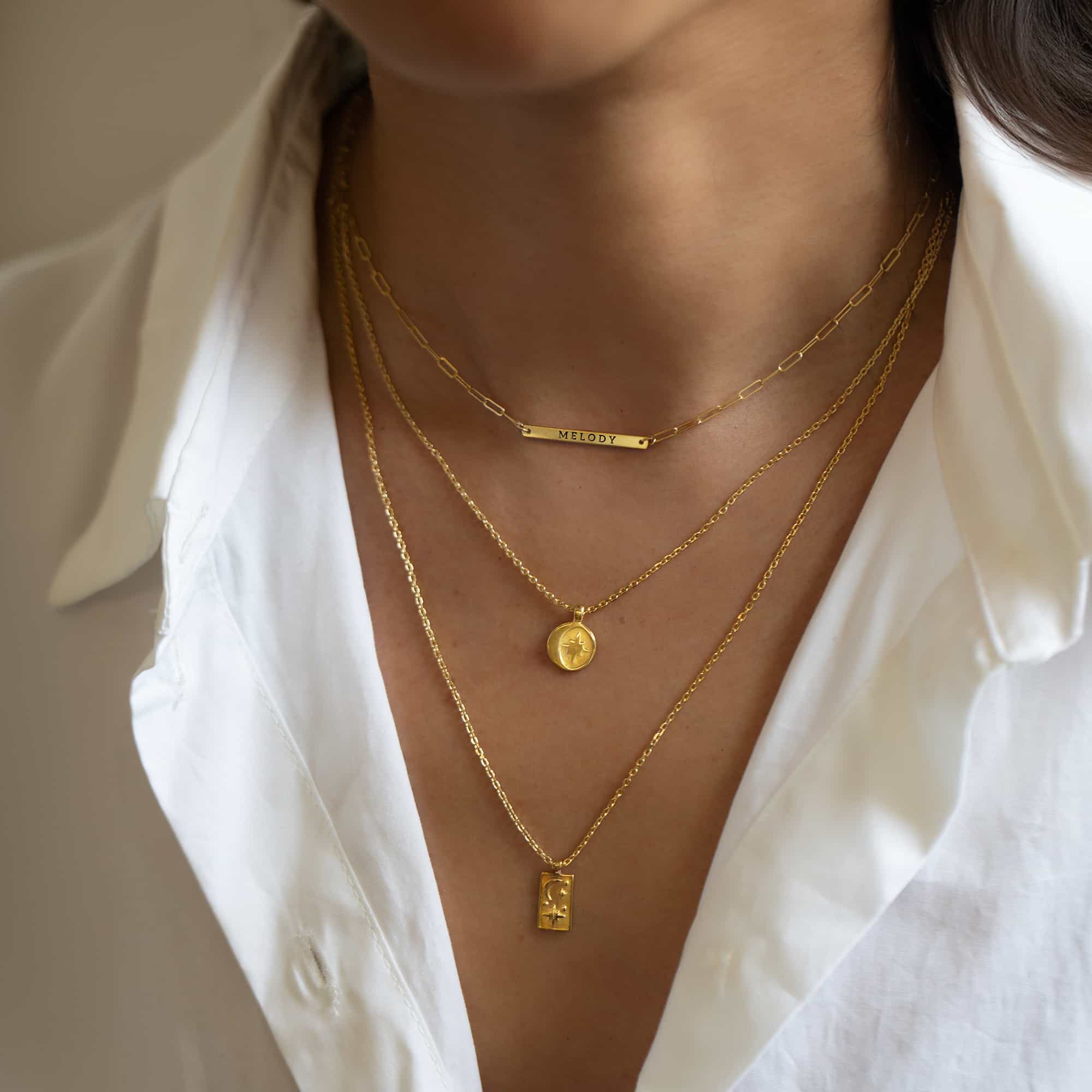 Layered gold necklaces on a model, including a bar engraved with a name, a star disc and a moon-and-star tag pendant
