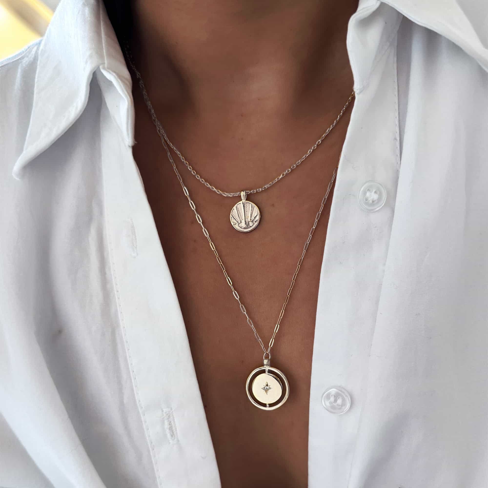 Silver round sunburst rays pendant layered with a gold pendant necklace, shown on a model's neckline