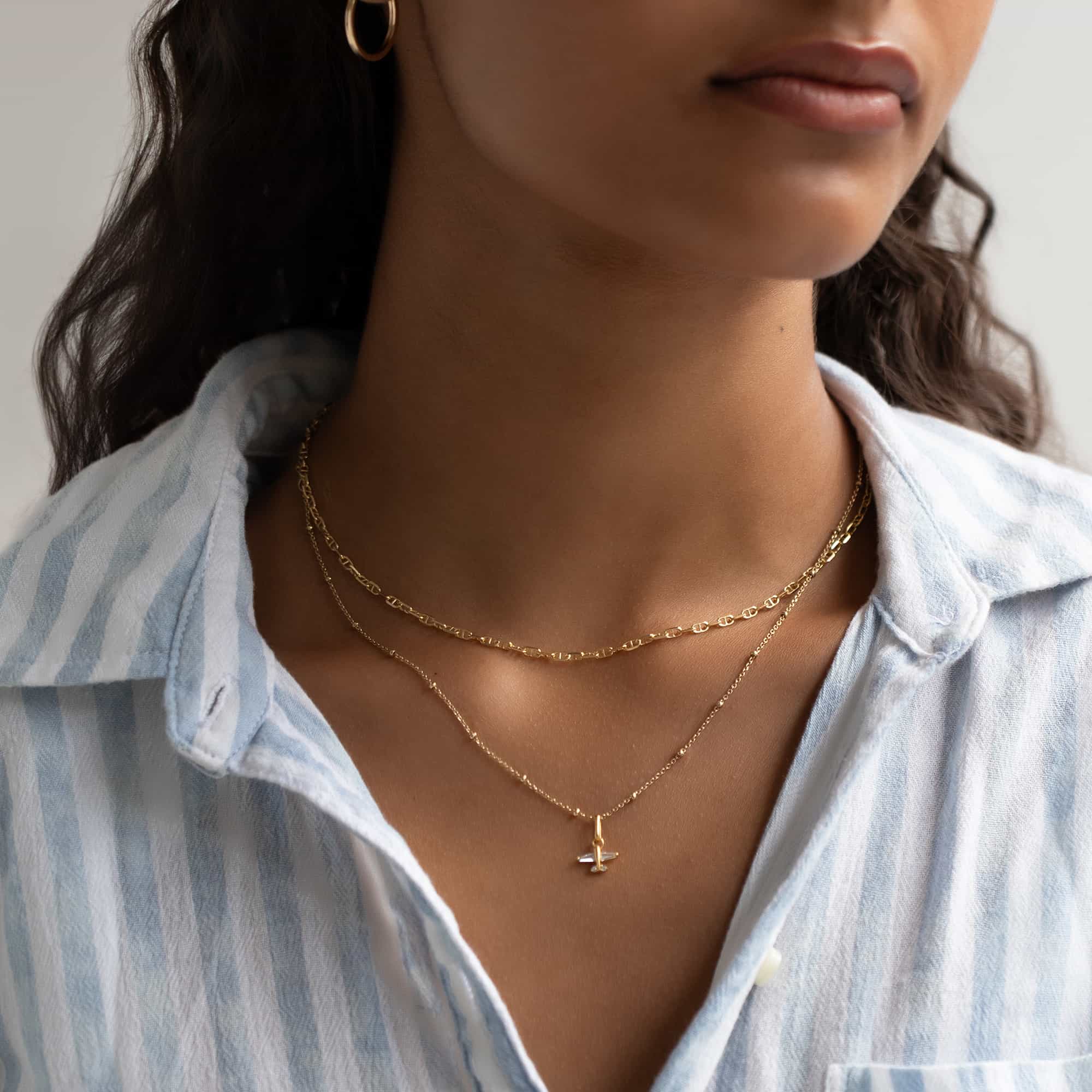 Gold vermeil airplane charm with a clear stone on a beaded chain, layered and shown on a model's neckline