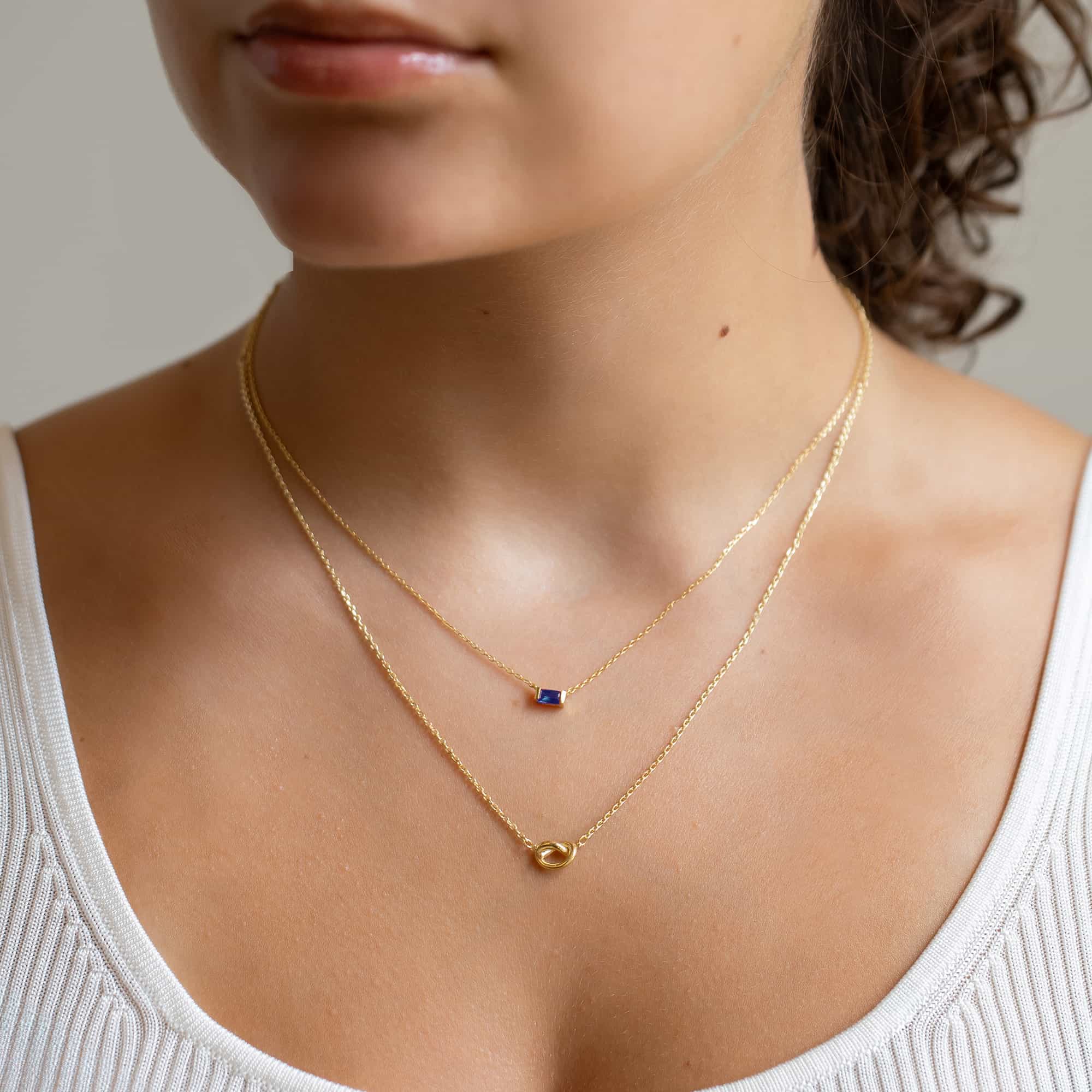 Gold vermeil layered duo with a blue baguette and a knot, shown on a model's neckline