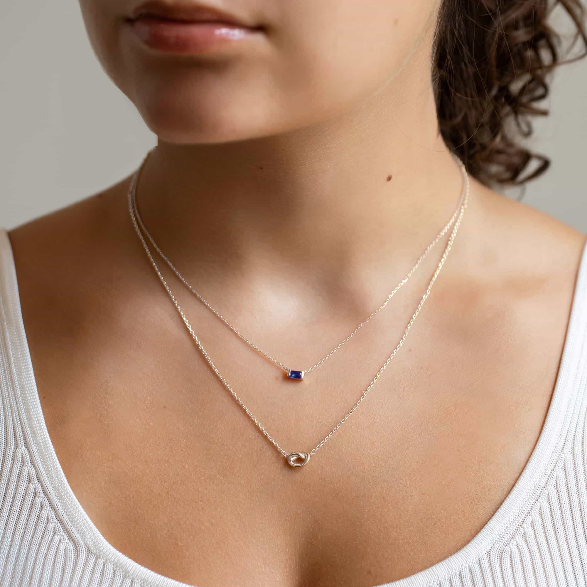 Sterling silver baguette blue sapphire and loveknot layered necklaces, shown on a model's neckline